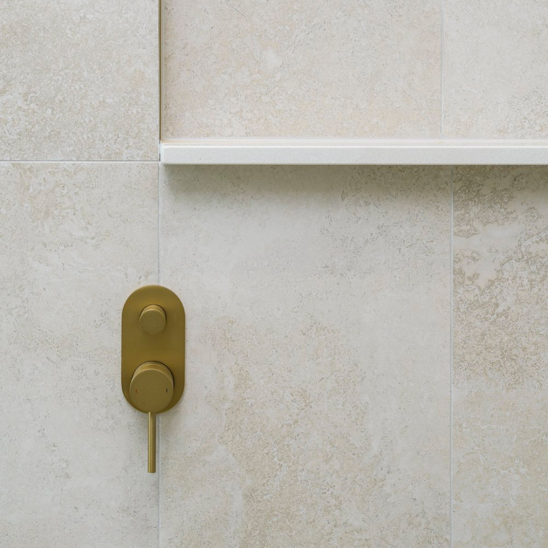 Close-up of a beige tiled wall with a brass shower control and a shelf above it.