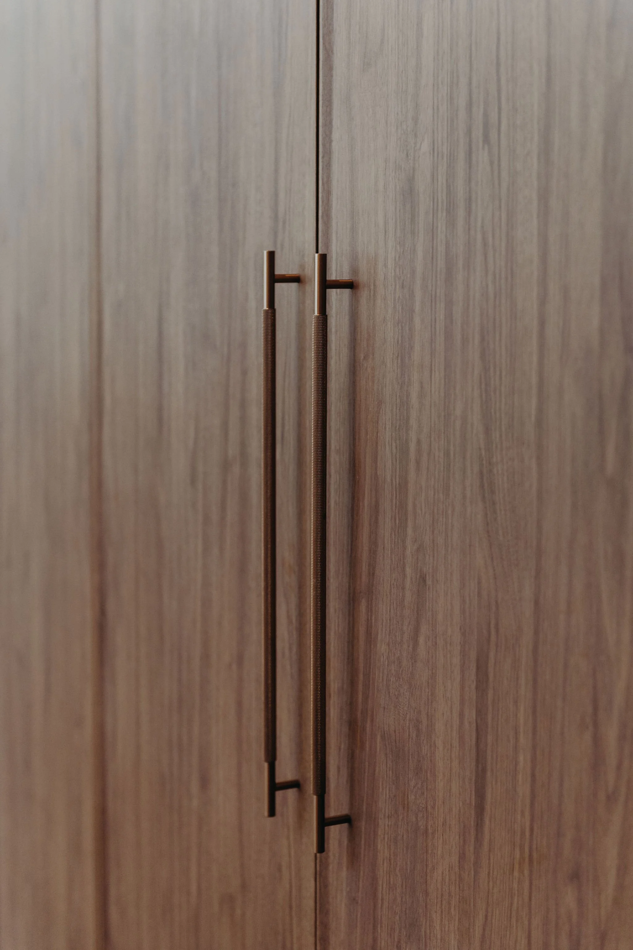 Close-up of a wooden cabinet with two vertical metal handles.