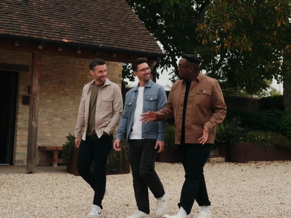 CODE Architects Partners are walking and talking outside near a brick building with a wooden roof and a tree with green leaves.