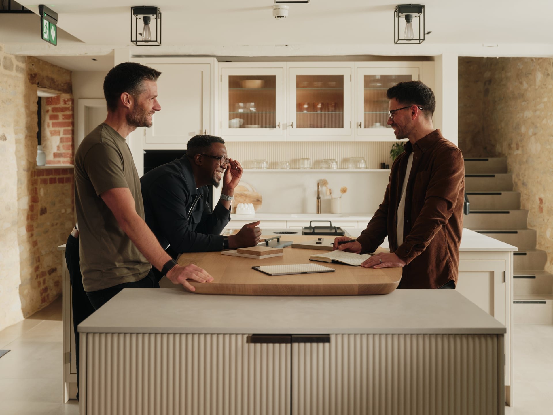 Three men laughing and talking around a kitchen island in a modern kitchen.
