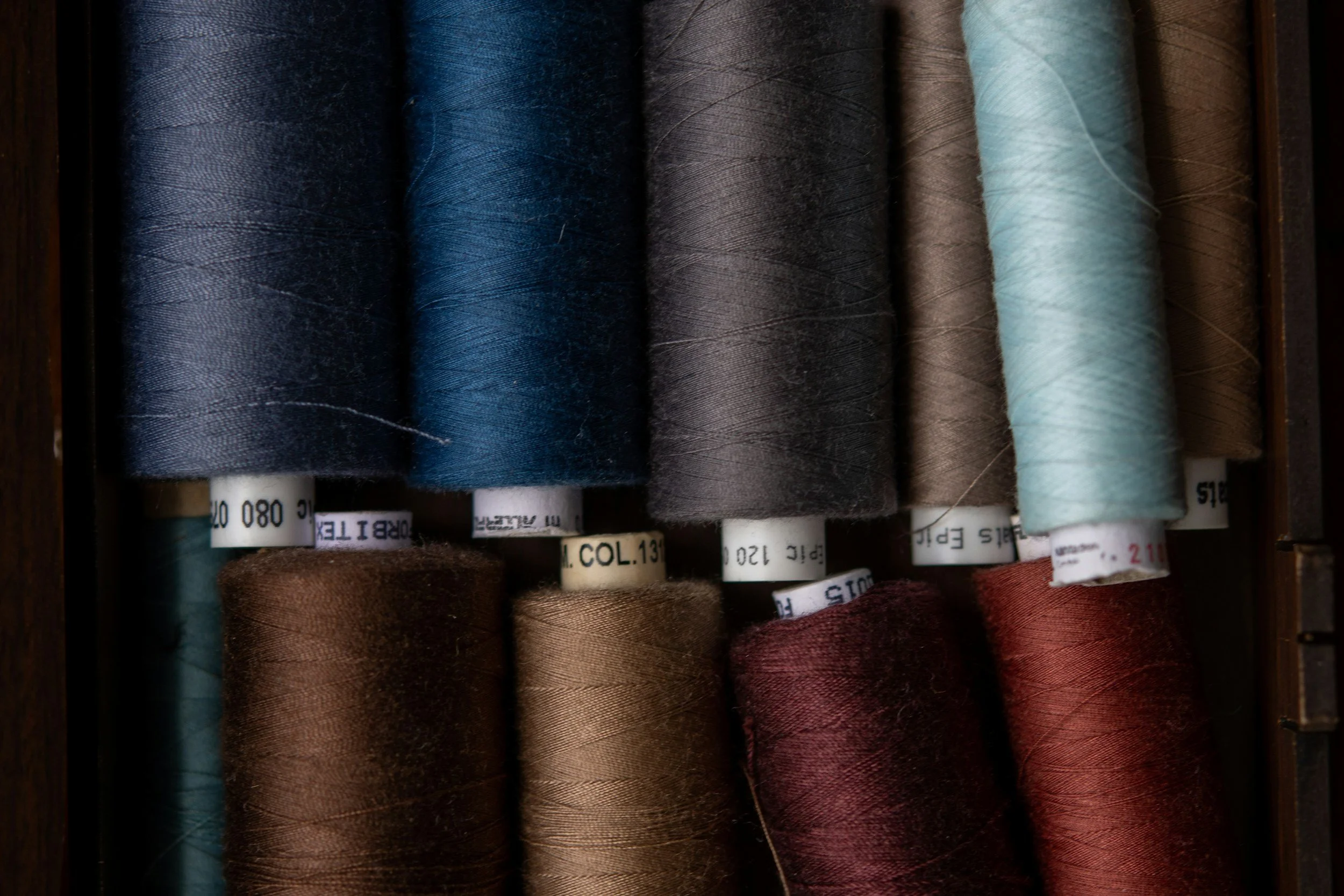 Spools of thread in various colors including dark blue, light blue, black, brown, and red arranged in a box.