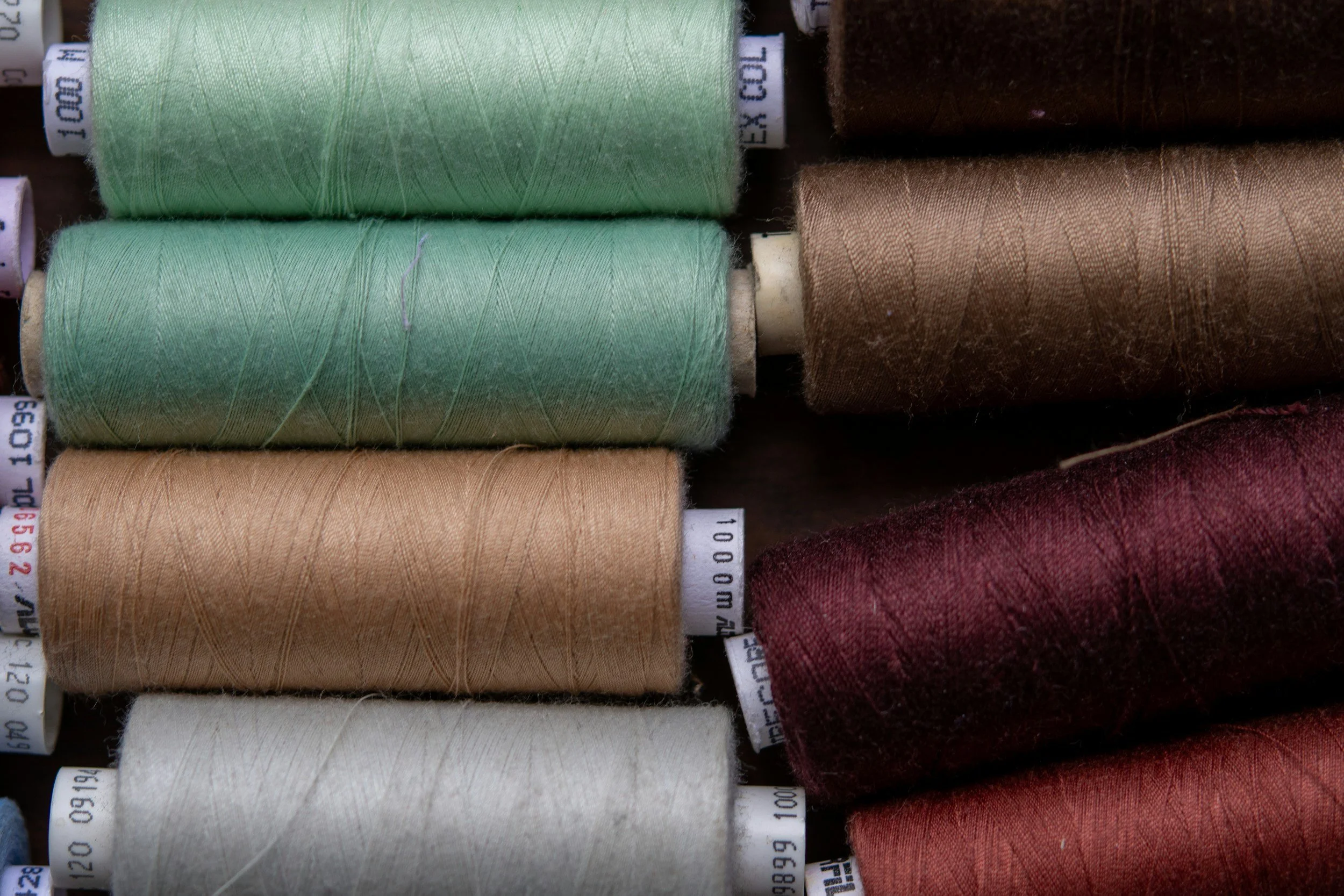Colored spools of thread in shades of green, brown, beige, white, and red arranged side by side.