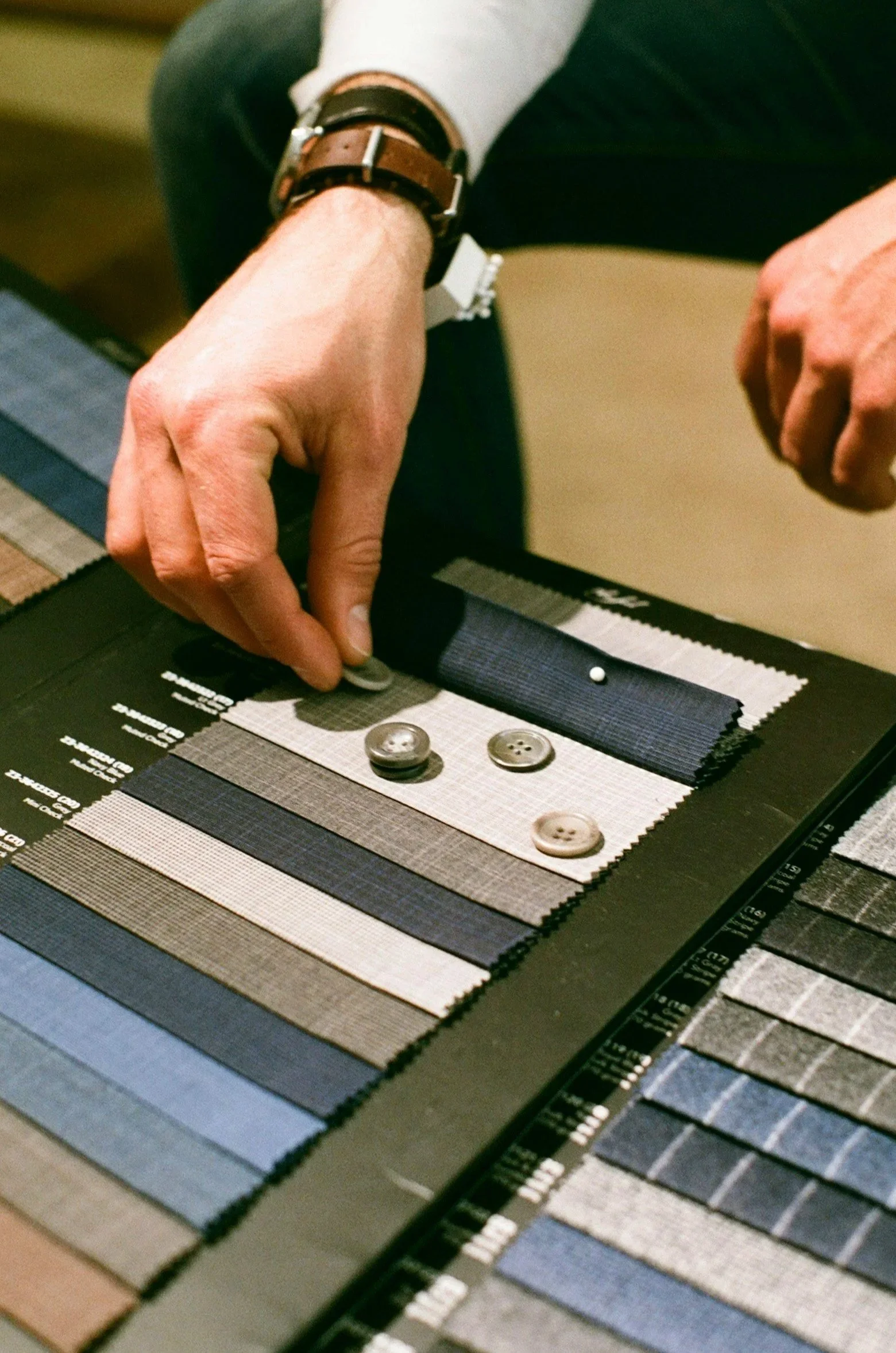 A person's hand selecting fabric swatches and buttons on a fabric sample book.