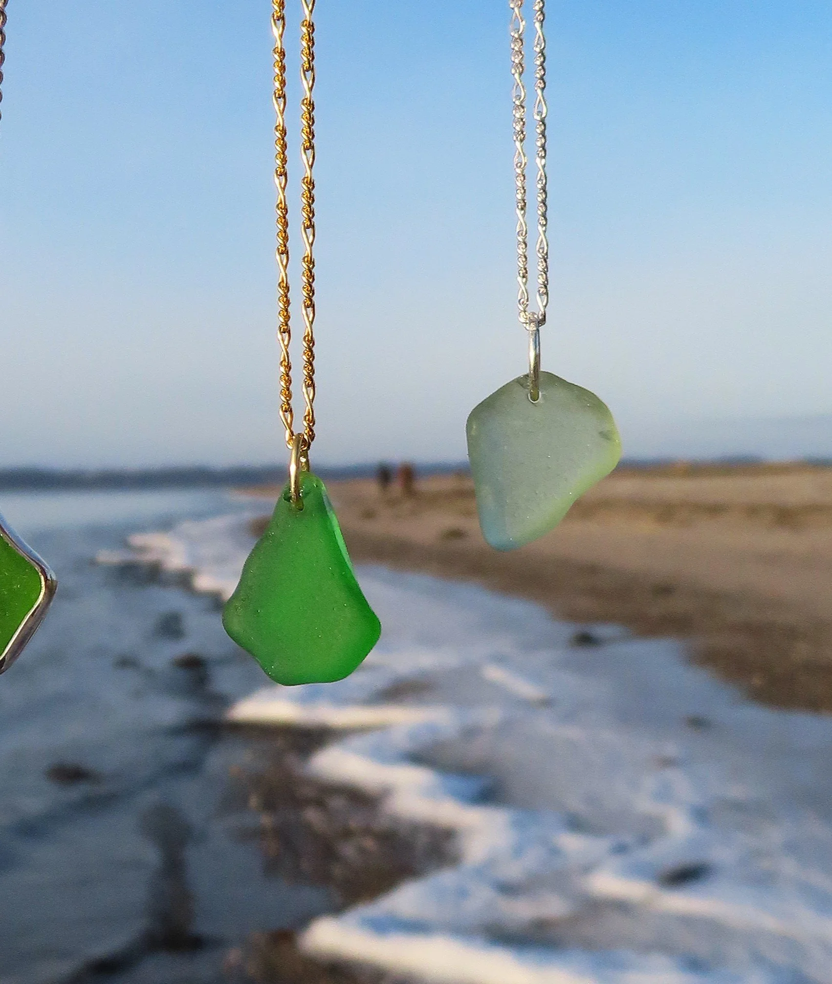 Billede af farverigt havglad med kæder, hængende foran en strand med hav og sand ved solnedgang med blå himmel.