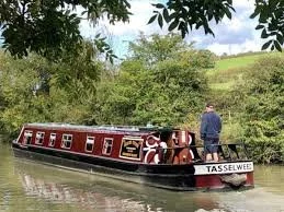 A narrowboat cruising slowly along the Grand Union Canal surrounded by peaceful countryside.
