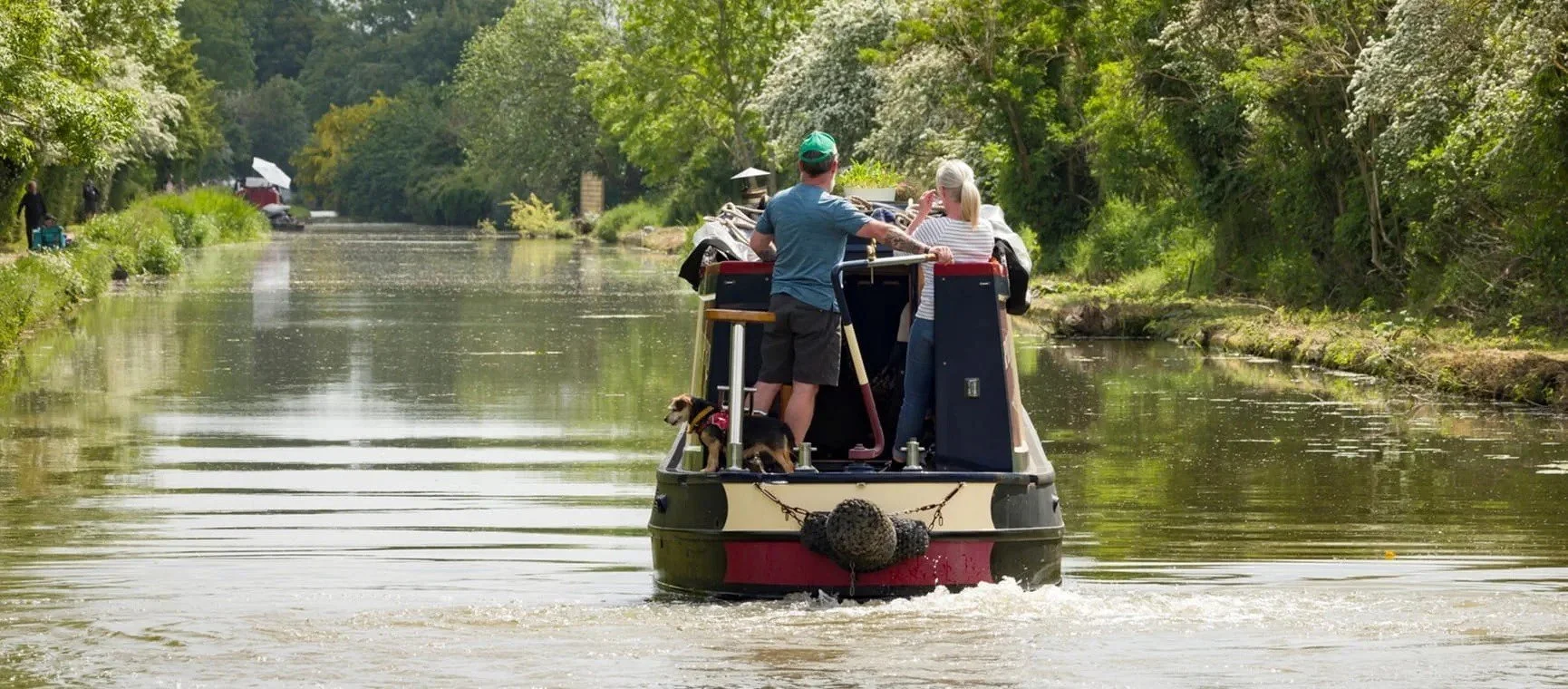 A first-time boater calmly steering a narrowboat along a peaceful stretch of the Grand Union Canal.