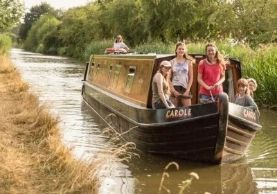 Beginners enjoying a relaxed narrowboat day hire on a calm stretch of the Grand Union Canal.