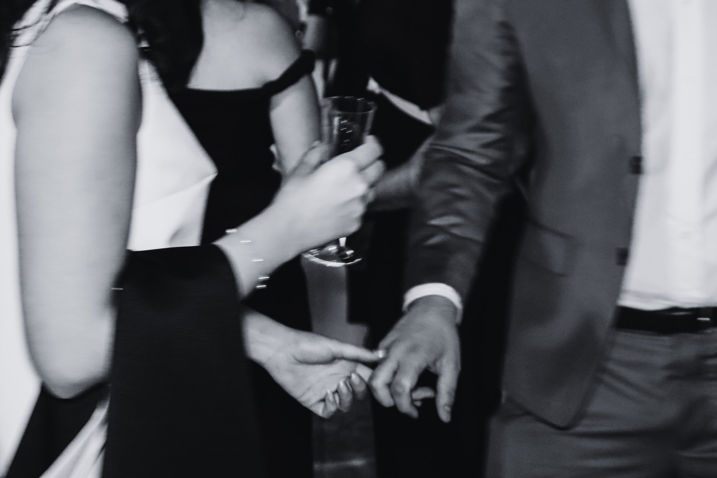 People holding hands and one person drinking from a glass during a social event.