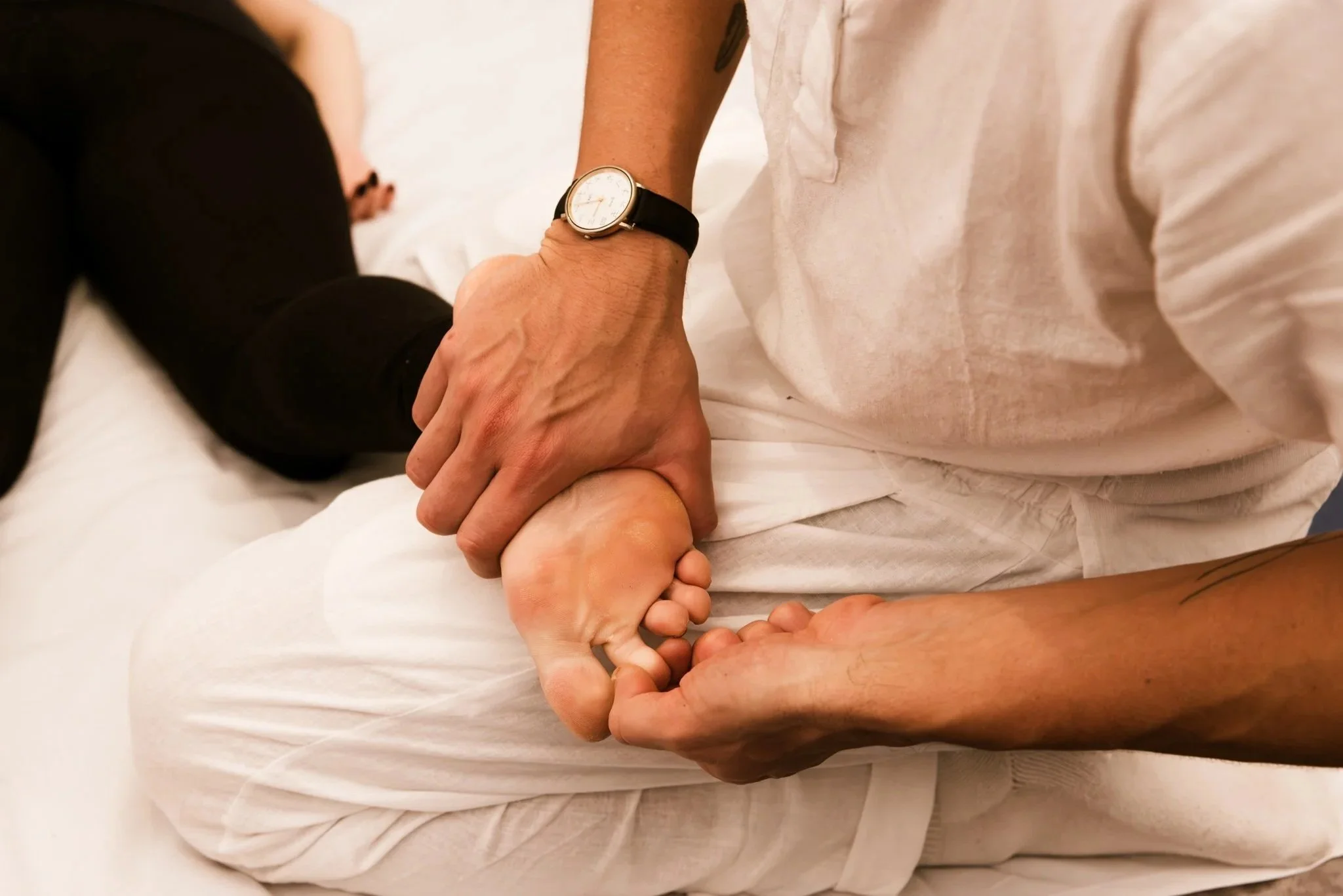 A person in white clothing is doing shiatsu on another person's foot.  The scene appears to be intimate and comforting.