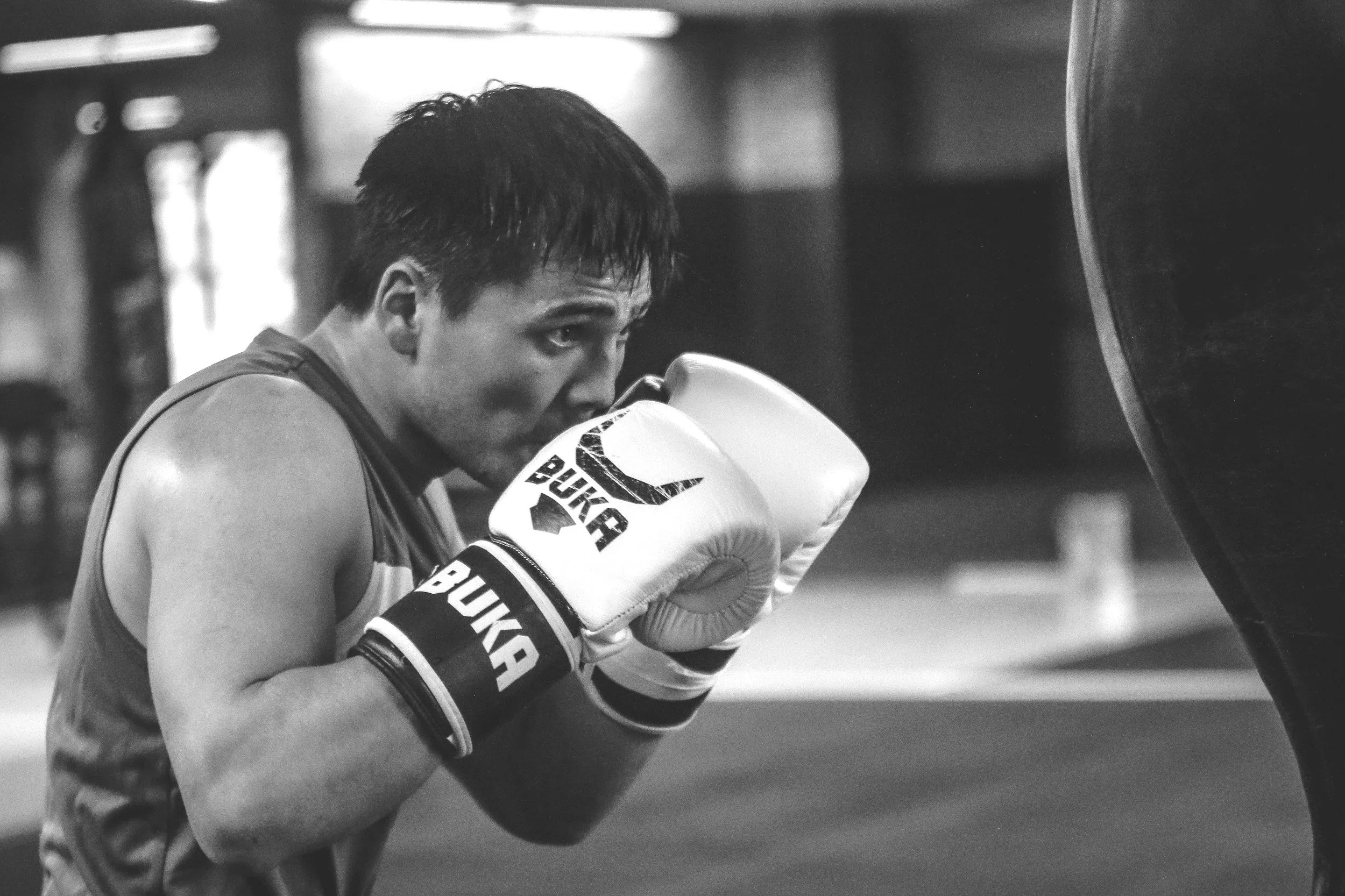 A male boxer wearing gloves and workout attire practicing boxing on a punching bag in a gym.