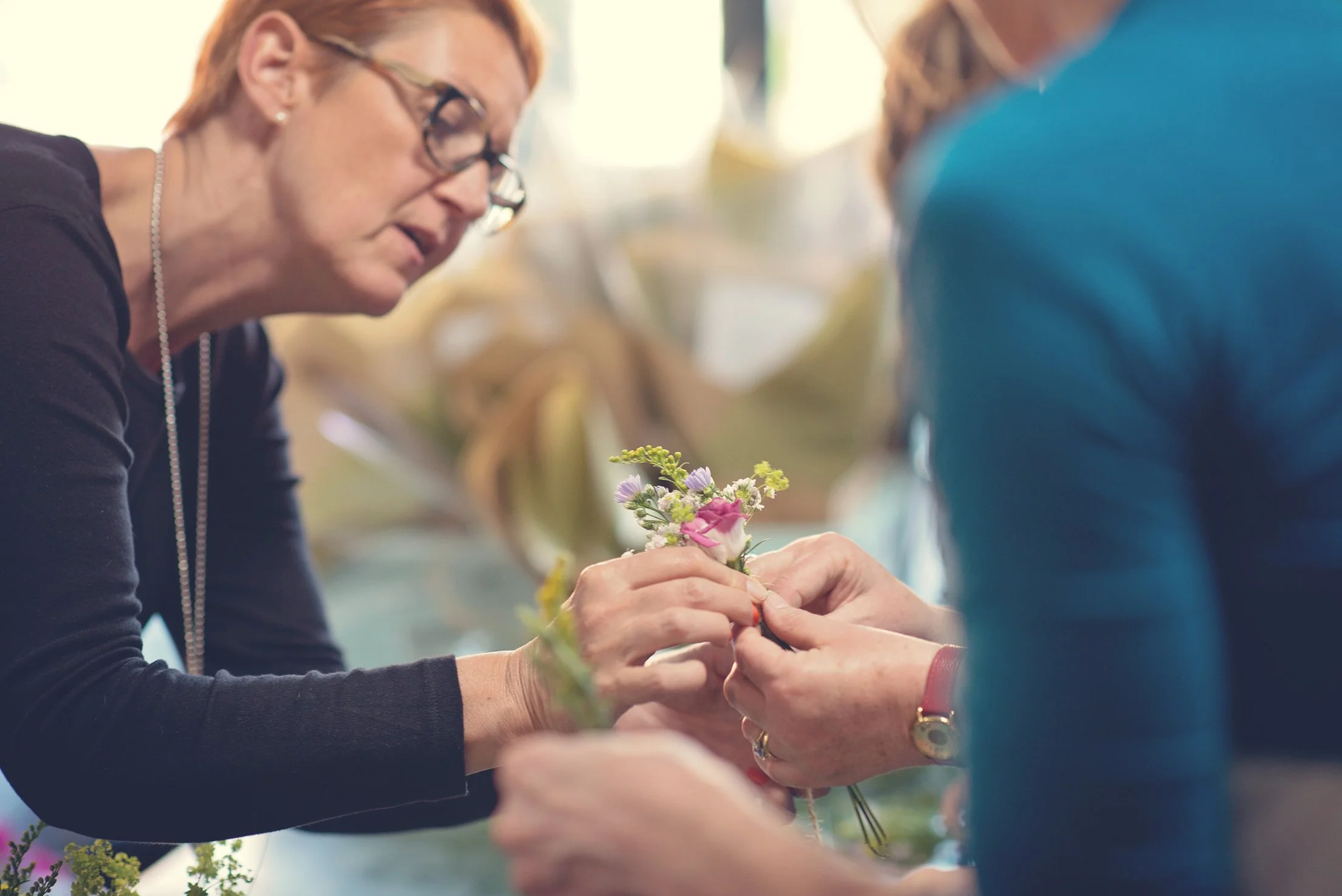 Two women are working together to assemble a small bouquet of flowers, focusing on adding the flowers.