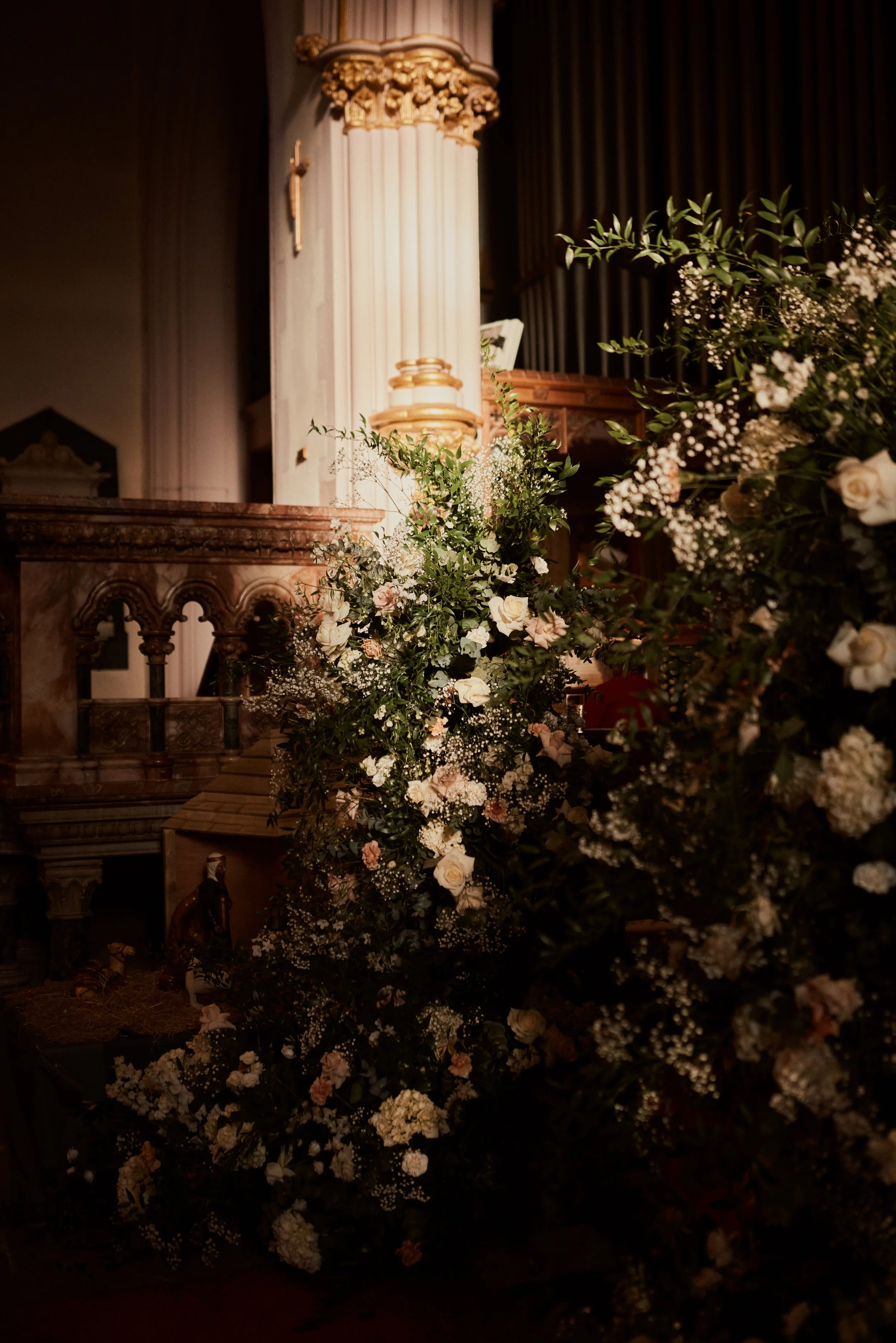 Indoor church altar decorated with a large freestanding floral installation of white and pink flowers and green foliage.