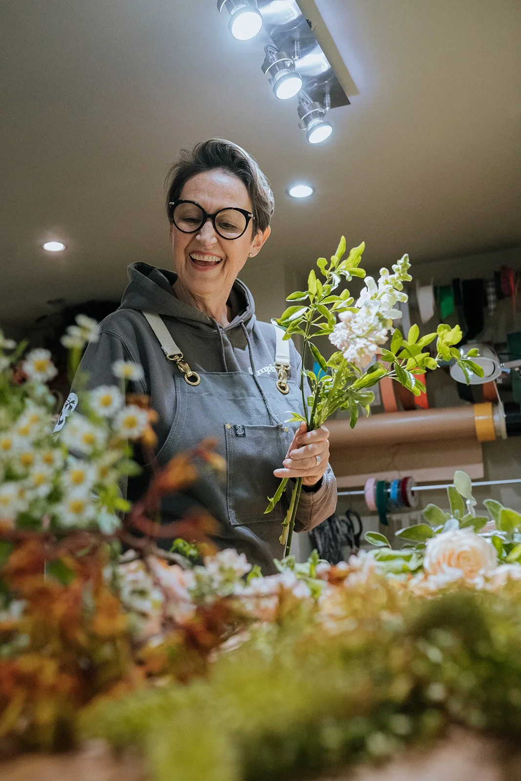 A woman with short hair and glasses demonstrates how to create a bridal flowers and a bridal bouquet in a workshop or floral shop.