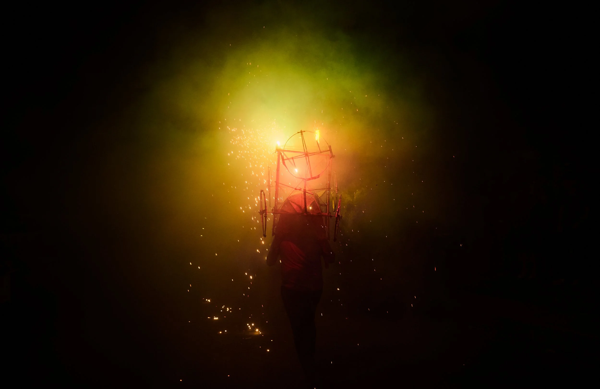 Persona sosteniendo una estructura de madera con fuegos artificiales en forma de círculo en la noche.