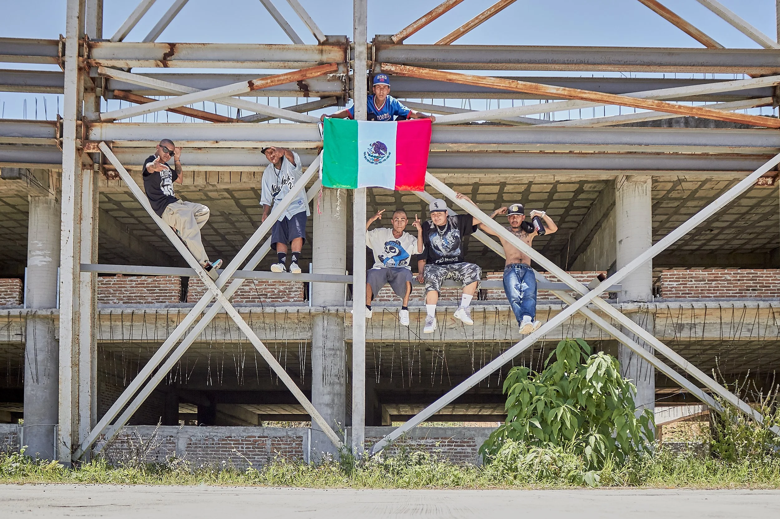 Grupo de jóvenes en una estructura de acero en construcción, uno de ellos sostiene una bandera de México.