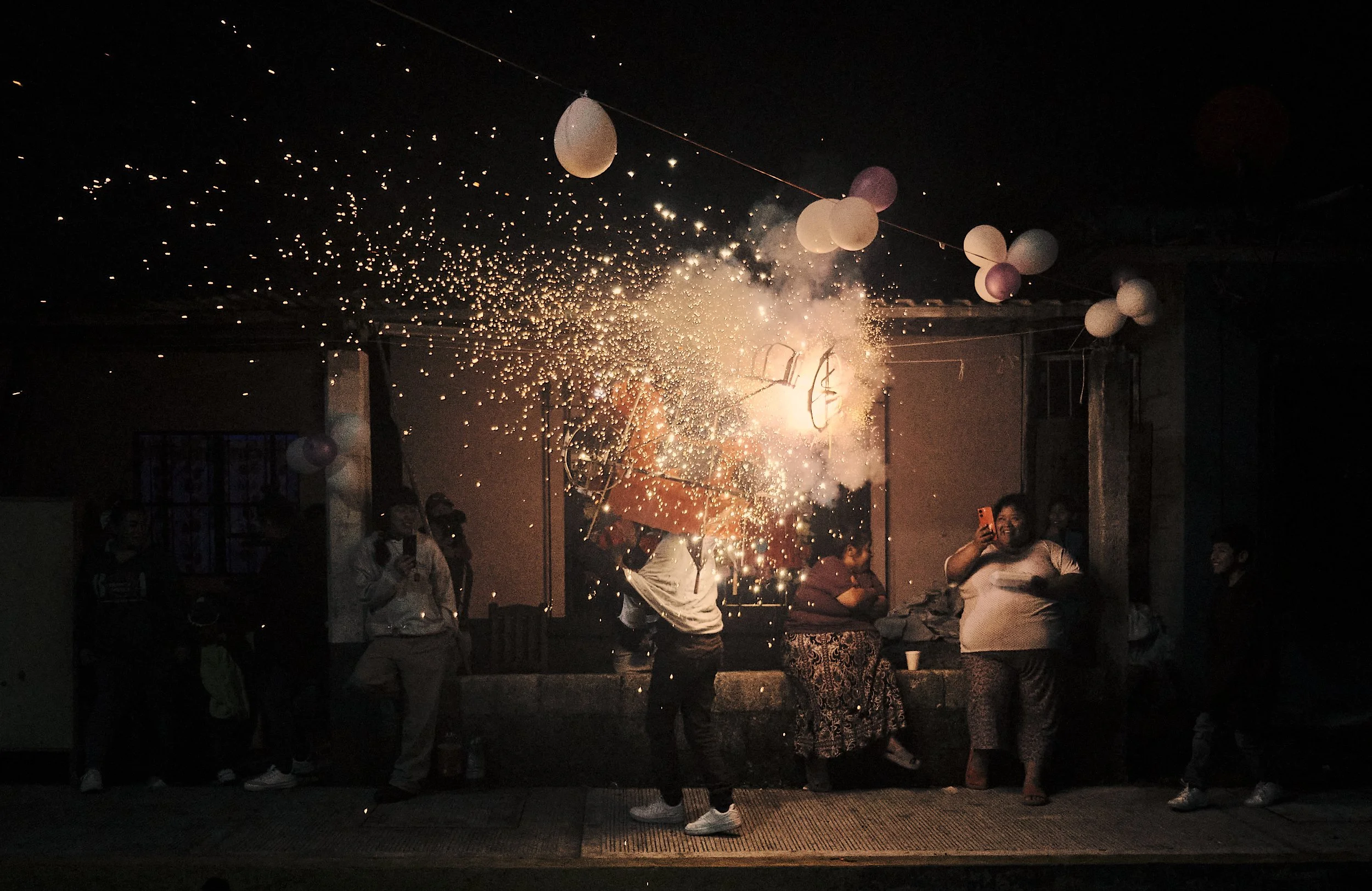 Grupo de personas celebrando en una fiesta con fuegos artificiales y globos en el techo.