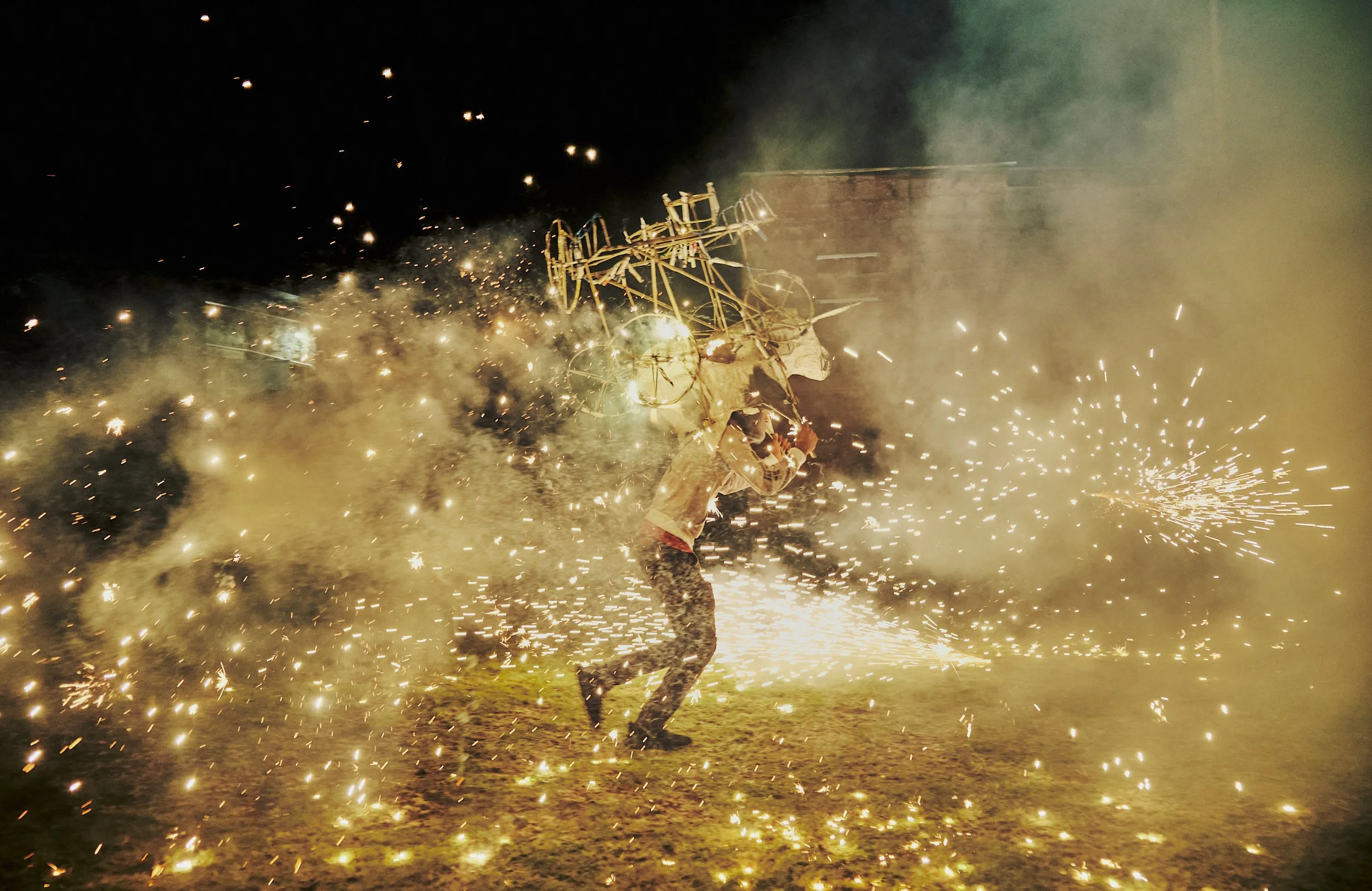 Persona quemando estructura de madera en medio de chispas y fuego durante la noche.