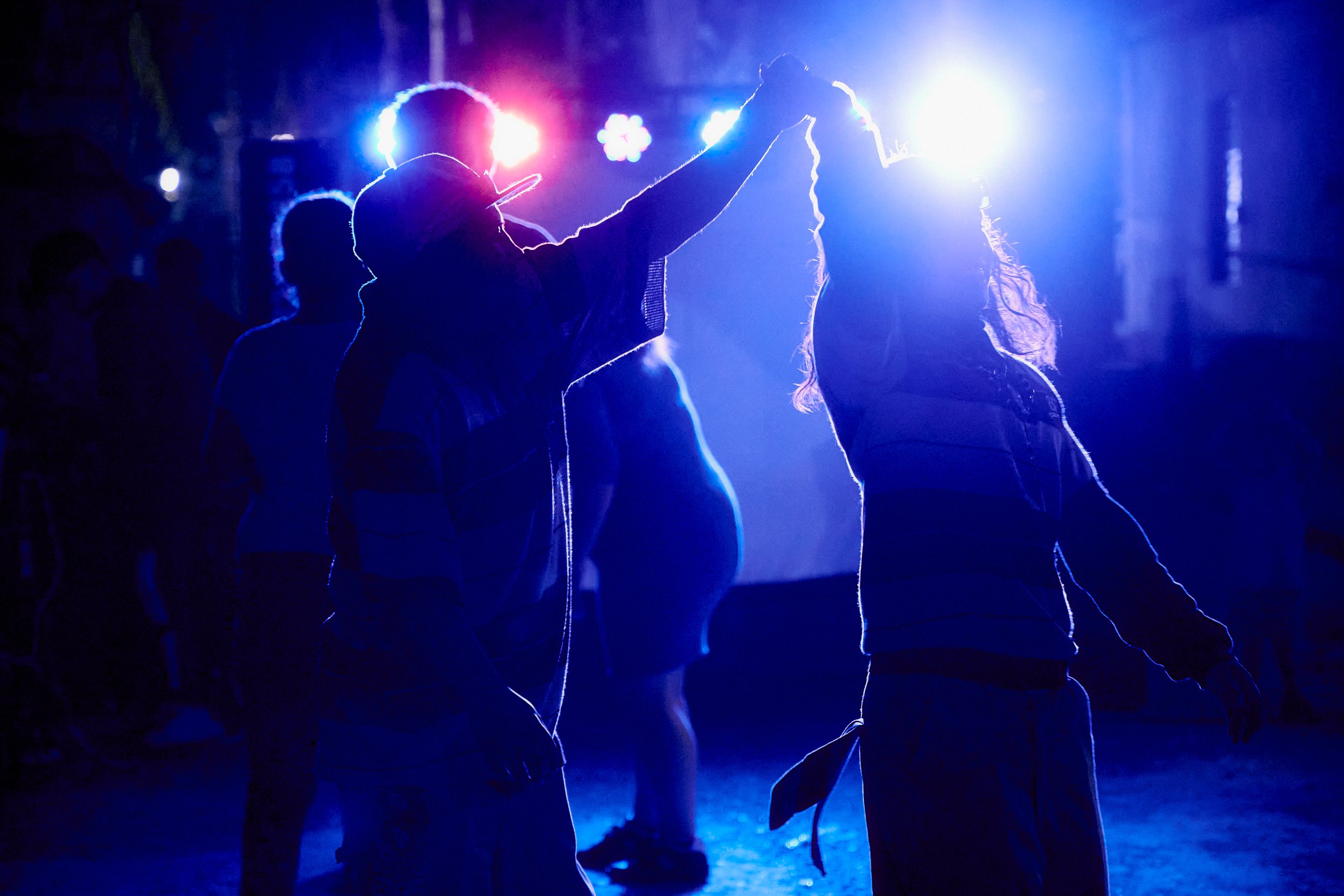 Silhouettes de personas bailando en un evento nocturno con luces brillantes de colores azules y rosas en el fondo.