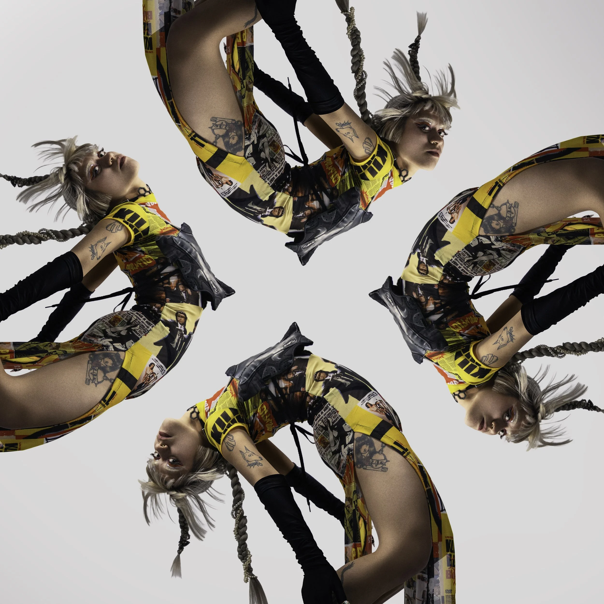 Multiple mirrored images of a woman in colorful printed dress, black gloves, and sneakers, with tattoos and braided hair, arranged in a kaleidoscopic pattern against a plain white background.