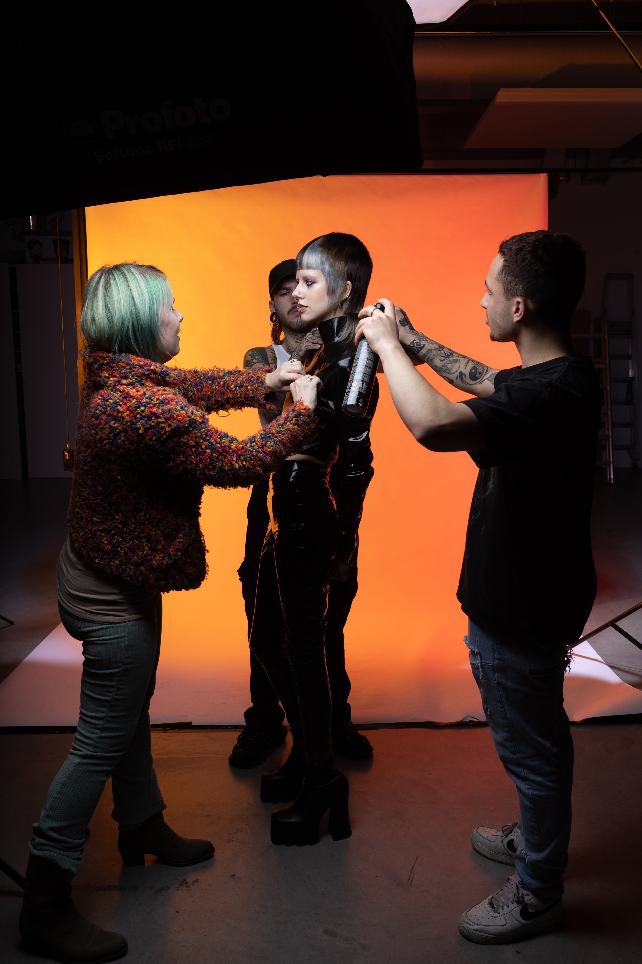 Fashion photoshoot with a model, hairstylist, and photographer in a studio with an orange backdrop
