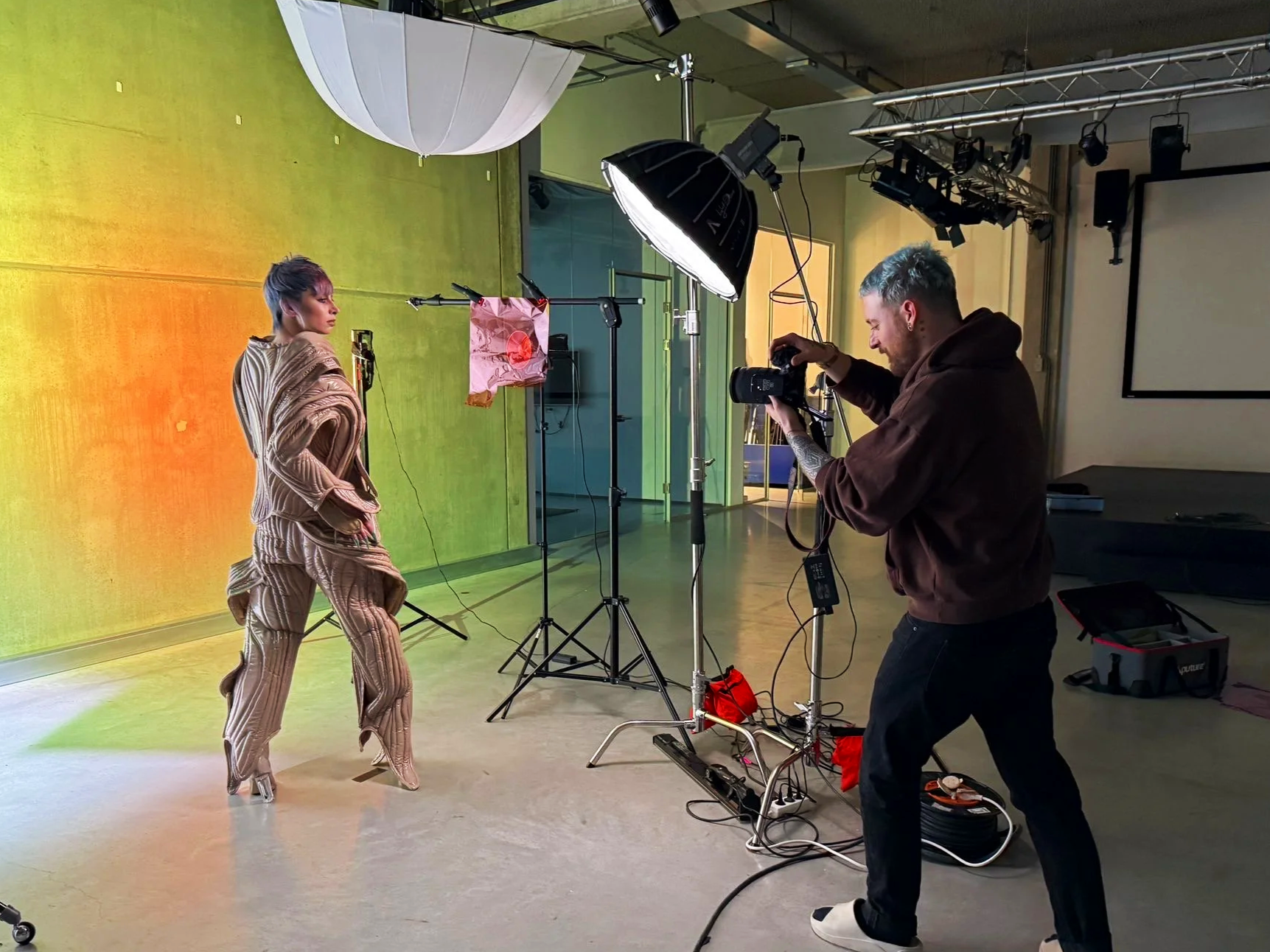 Photographer taking pictures of a model in a studio with colorful backdrops and professional lighting equipment.