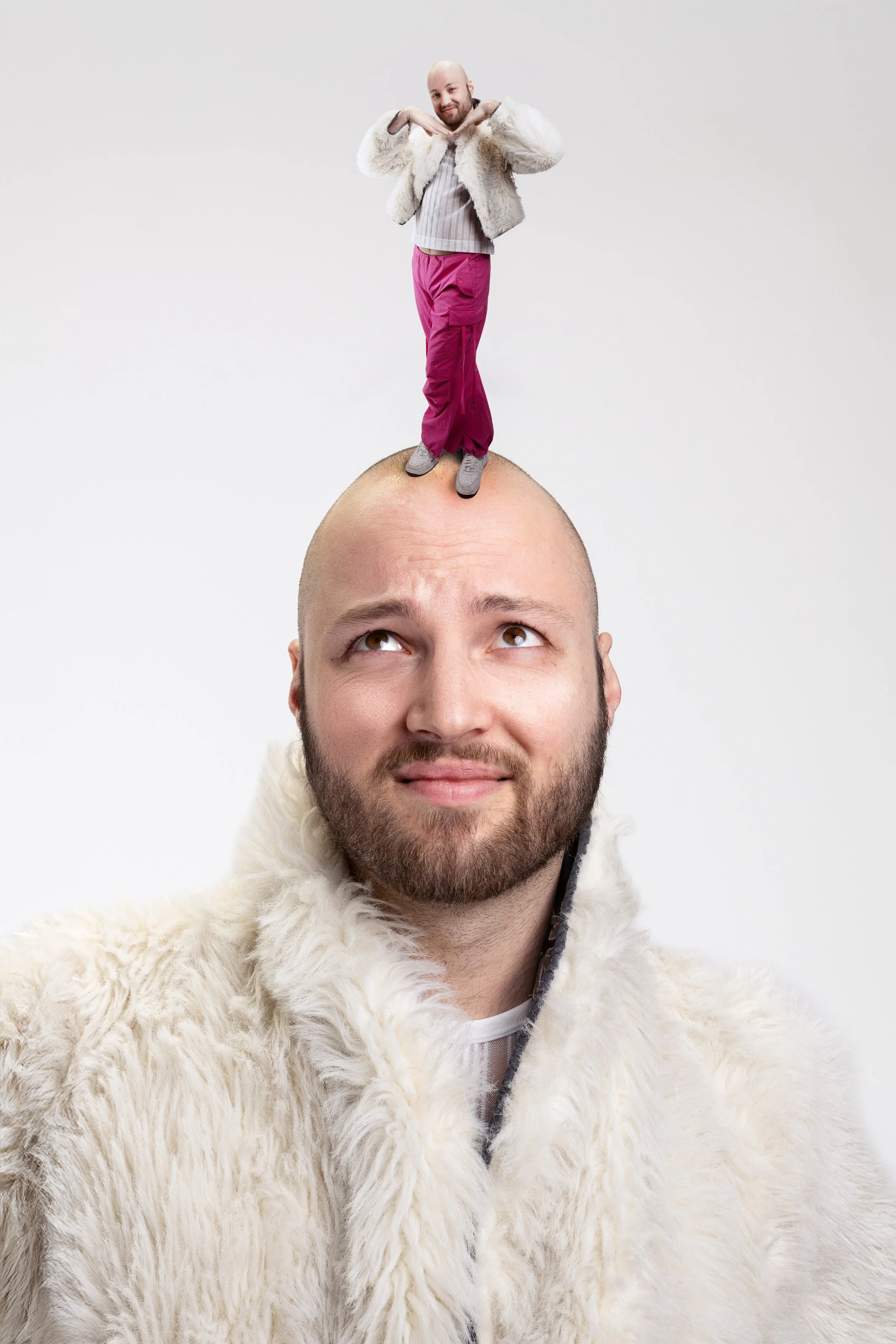 A man with a beard and bald head wearing a white furry coat, looking up and smiling, with a smaller person standing on his head, wearing a white fur jacket, pink pants, and gray shoes, making a playful gesture.