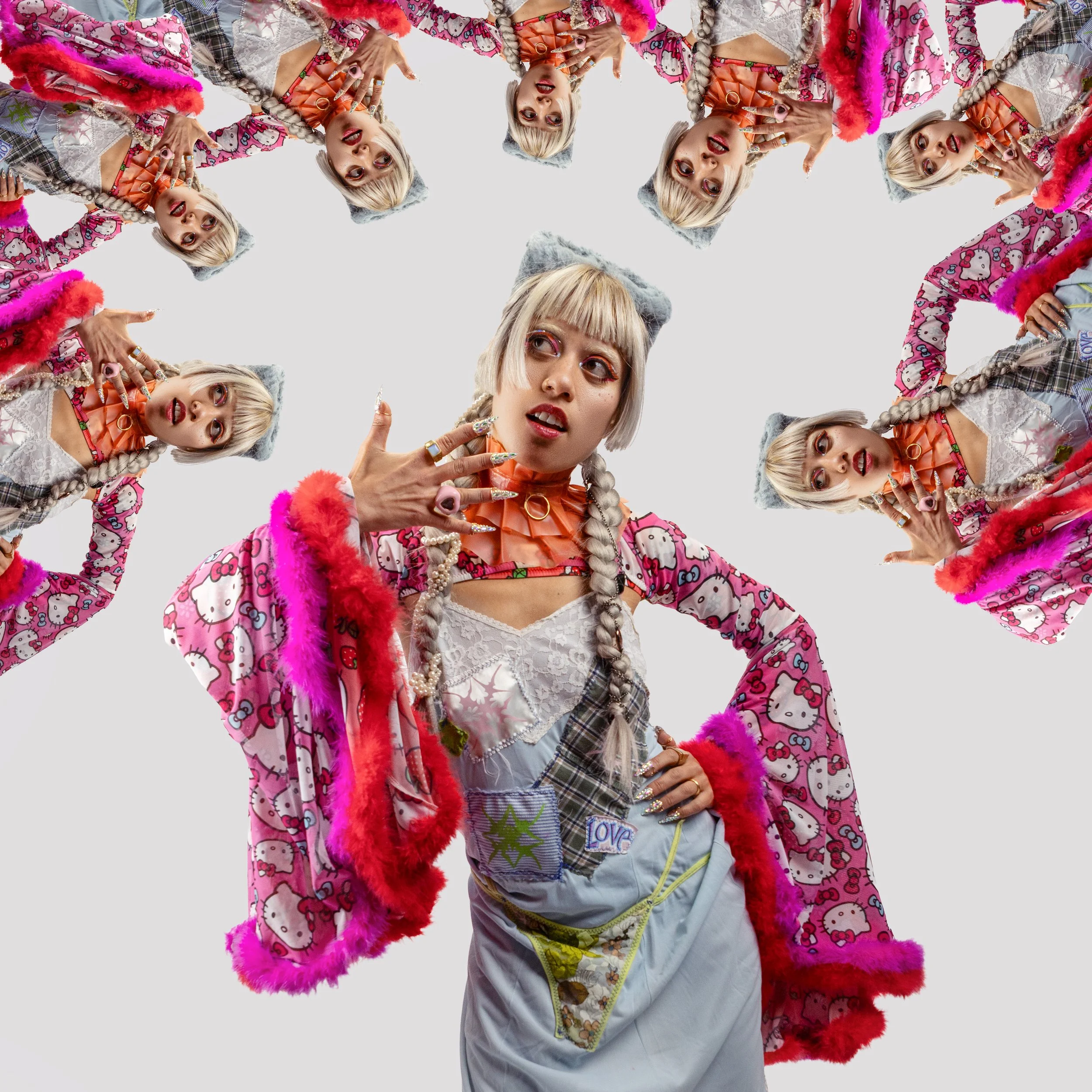 A woman with platinum blonde hair styled in braids, wearing colorful, eccentric clothing including a pink Hello Kitty patterned cape, a gray beret, and various jewelry, posing with her hand near her face. Multiple copies of her are arranged in a circ