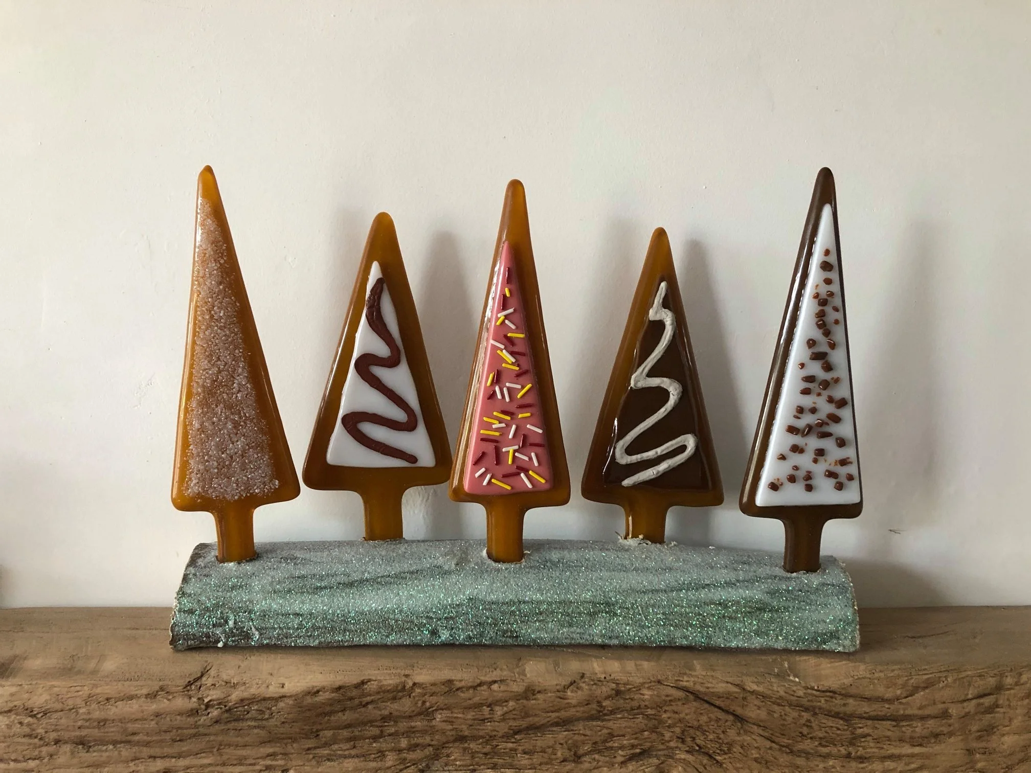 Decorative holiday trees made of baked goods with colorful icing and sprinkles displayed on a wooden surface.