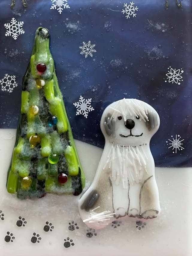 Decorative Christmas cookies shaped like a Christmas tree and a dog, placed on snow-themed paper with snowflake and paw print designs.