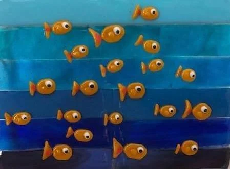 Small orange fish with large eyes swimming in a brightly colored ocean or tank with multiple shades of blue.