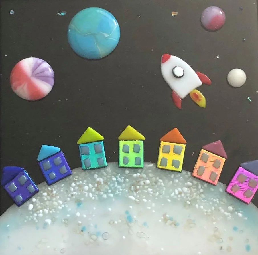 Colorful clay houses, planets, and a rocket ship on a black background, creating a space and neighborhood scene.