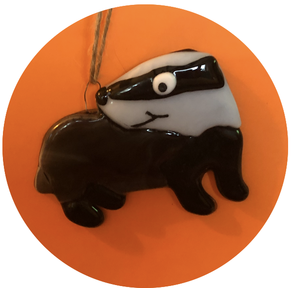 A black and white glass or ceramic ornament of a raccoon, hanging by a string against an orange background.