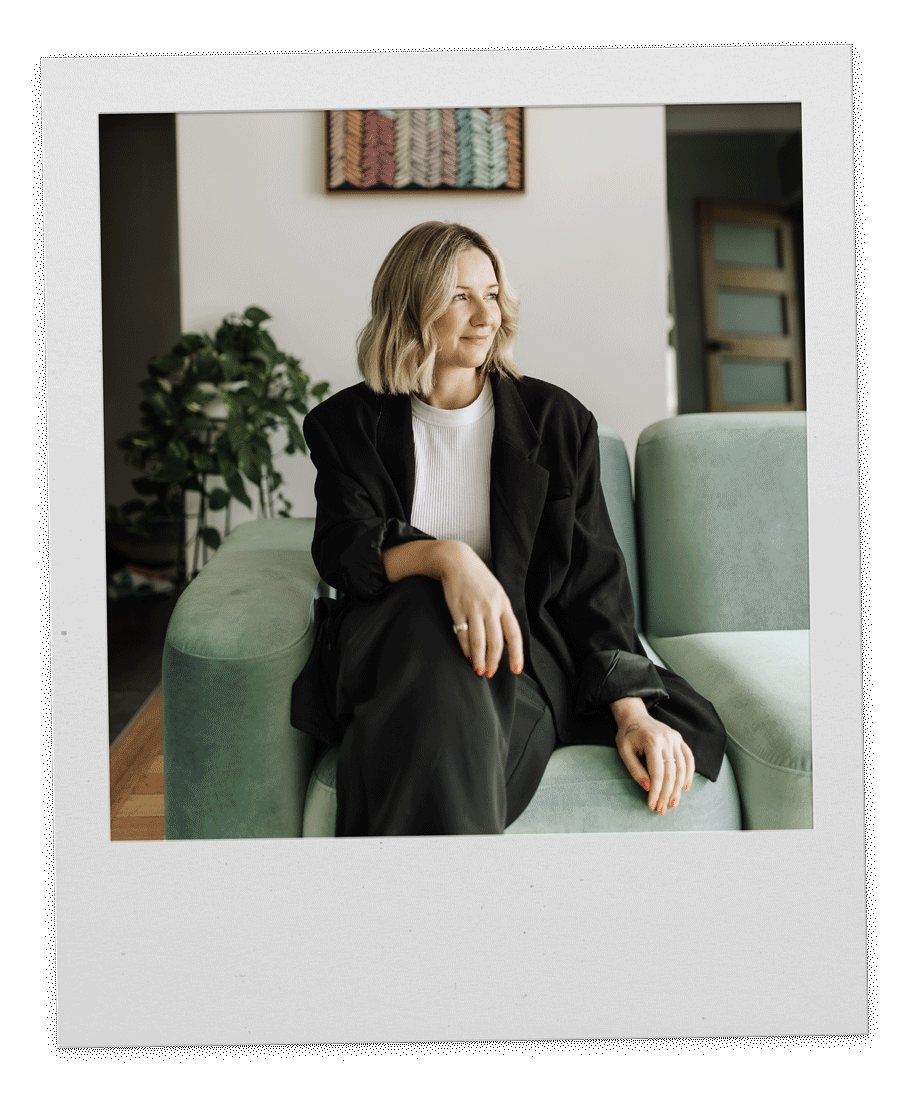 Woman with blonde hair sitting on a green sofa in a warmly lit room, looking to the side.