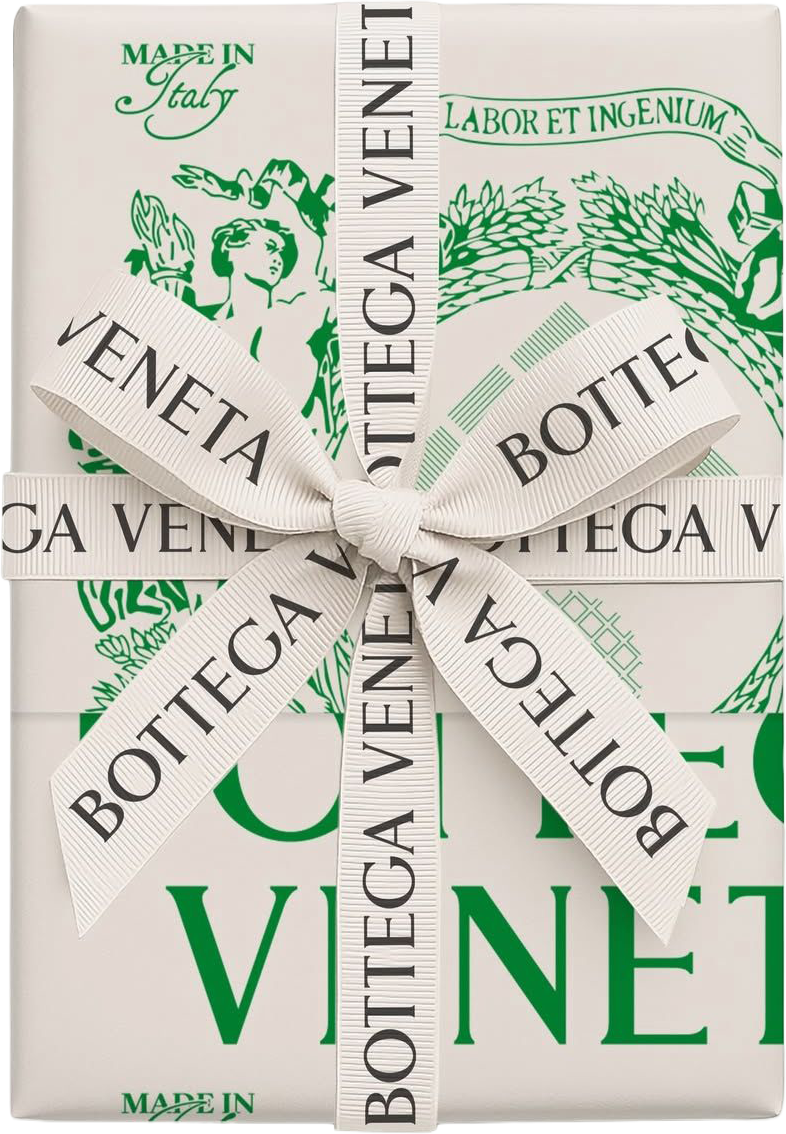 A white gift box with green and black text, wrapped with a white ribbon tied in a bow. The ribbon has 'Bottega Veneta' written on it. The box features design elements including leaves, a woman, and the text 'Made in Italy' and 'Labor et Ingenium'.