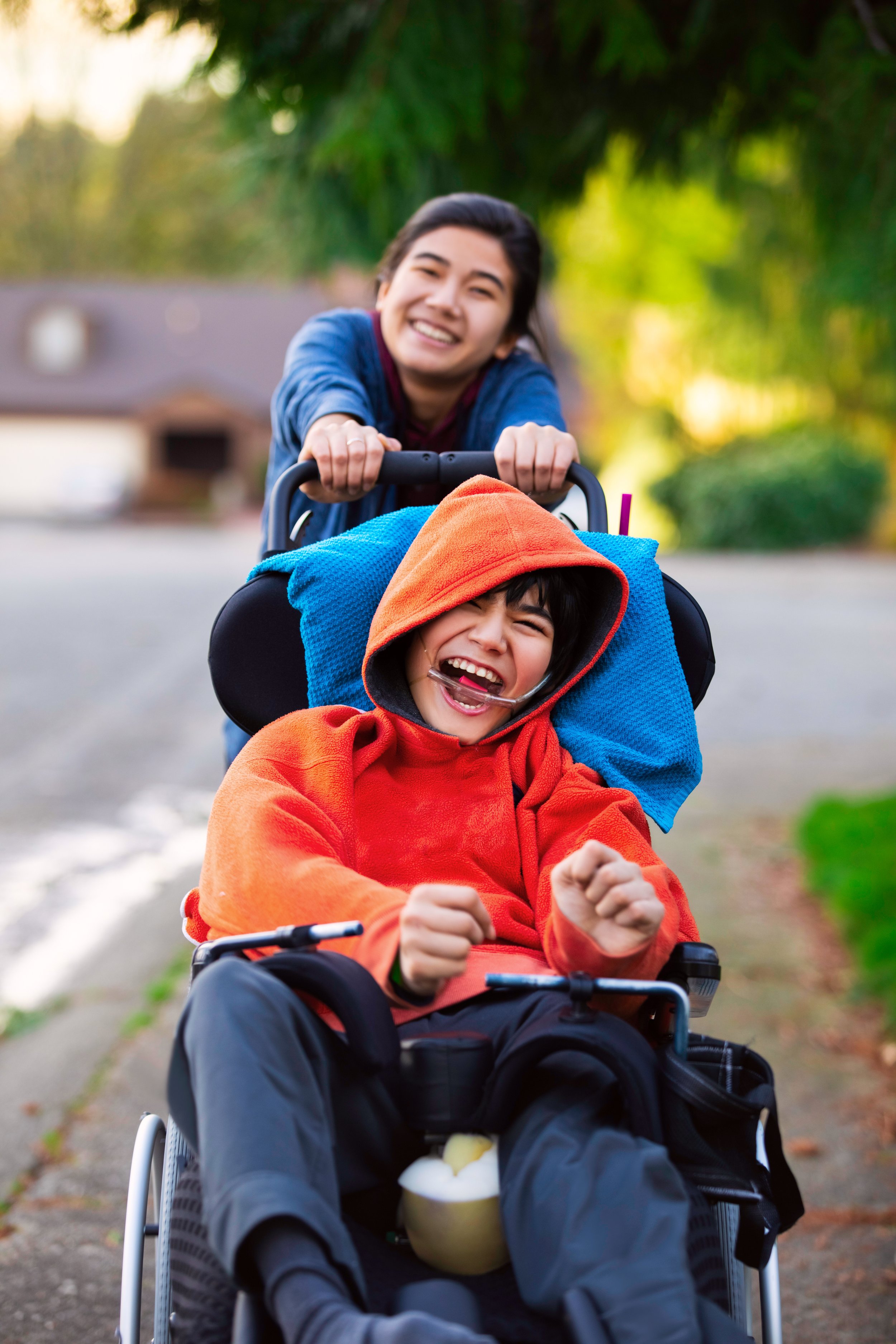 A young woman pushing an autistic boy in a wheelchair during a fall walk, both smiling.