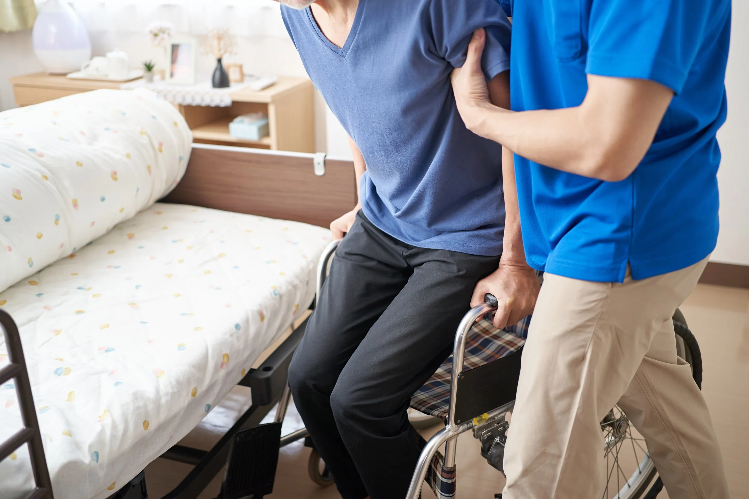 A person in a hospital bed being assisted to sit up by a nurse or caregiver in a healthcare facility.