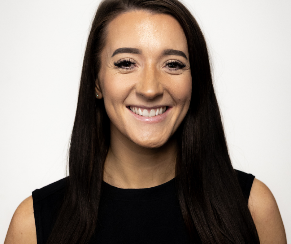 Megan Dente, coach at Barbelle smiling, wearing a black top with white accents, against a plain white background.