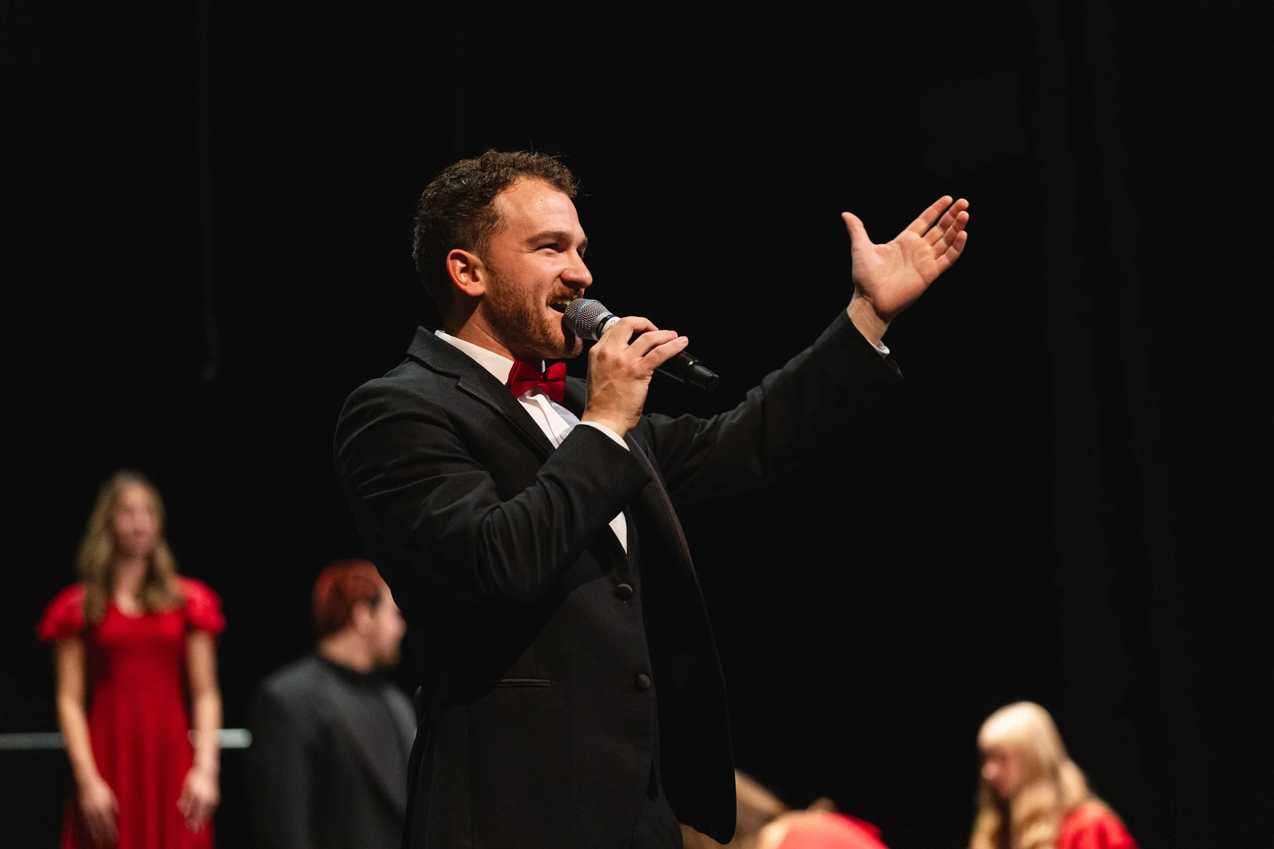 A young man with short, dark brown hair and a light beard, smiling and showing his teeth.