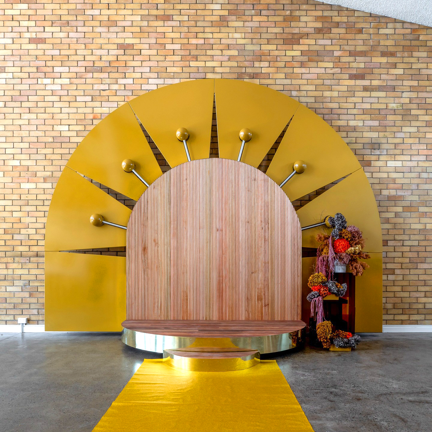 The Chapel Port Kembla - Wedding Venue Illawarra. Decorative backdrop with large mustard-yellow semi-circular structure, gold and wooden accents.