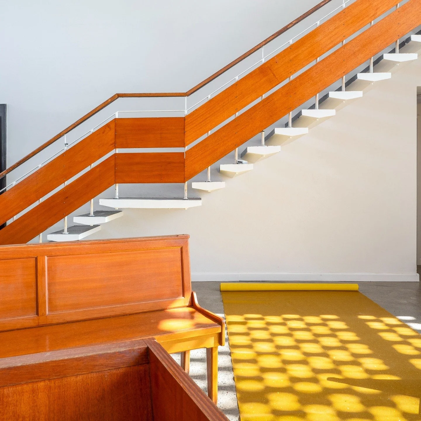 The Chapel Port Kembla - Wedding Venue Illawarra. Interior of a building with a wooden staircase, a wooden bench, and a yellow carpet with sunlight creating a pattern of circles.