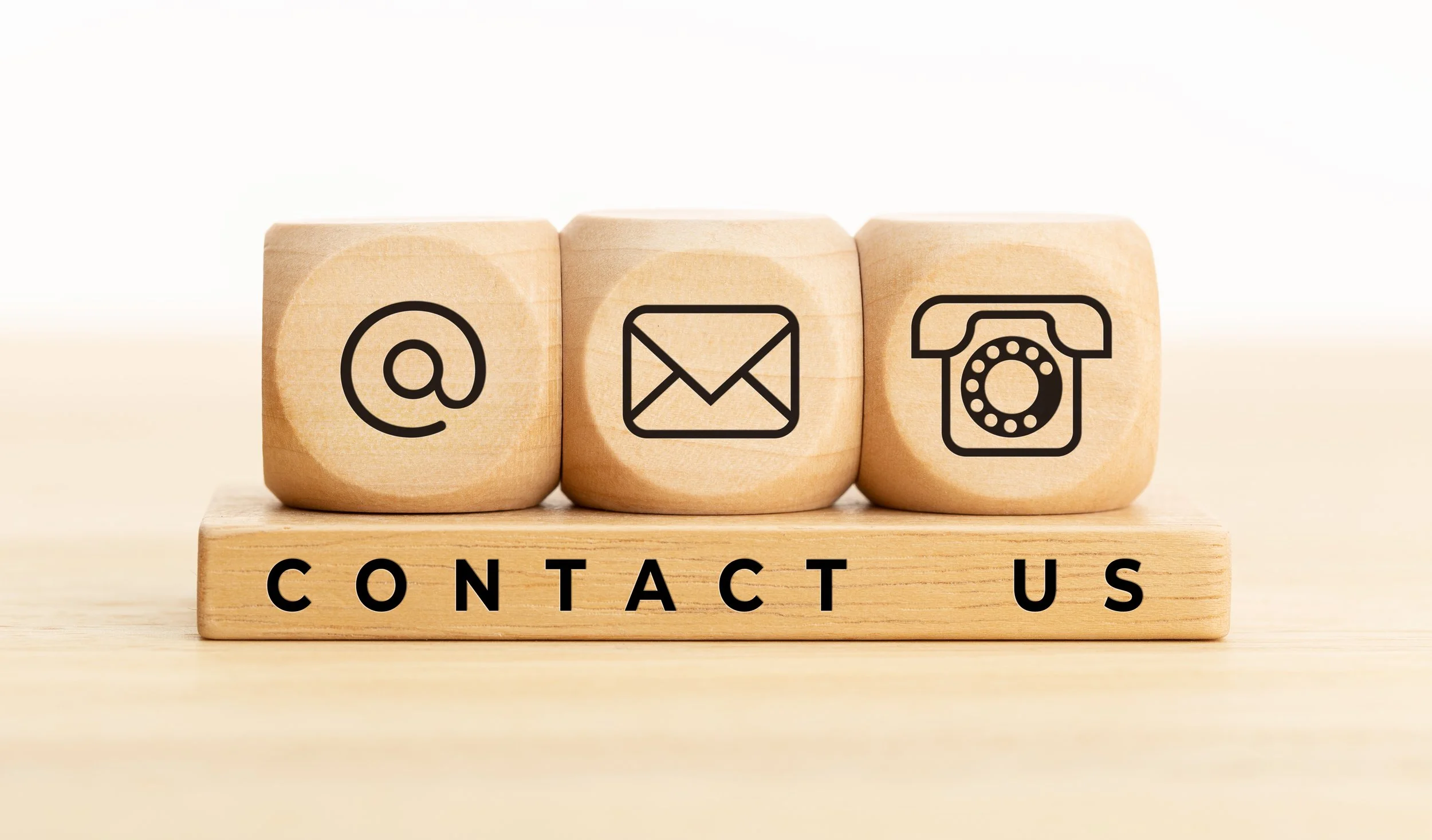 Three wooden blocks with contact icons: at symbol, email, and phone, placed on a wooden base with 'CONTACT US' written below.
