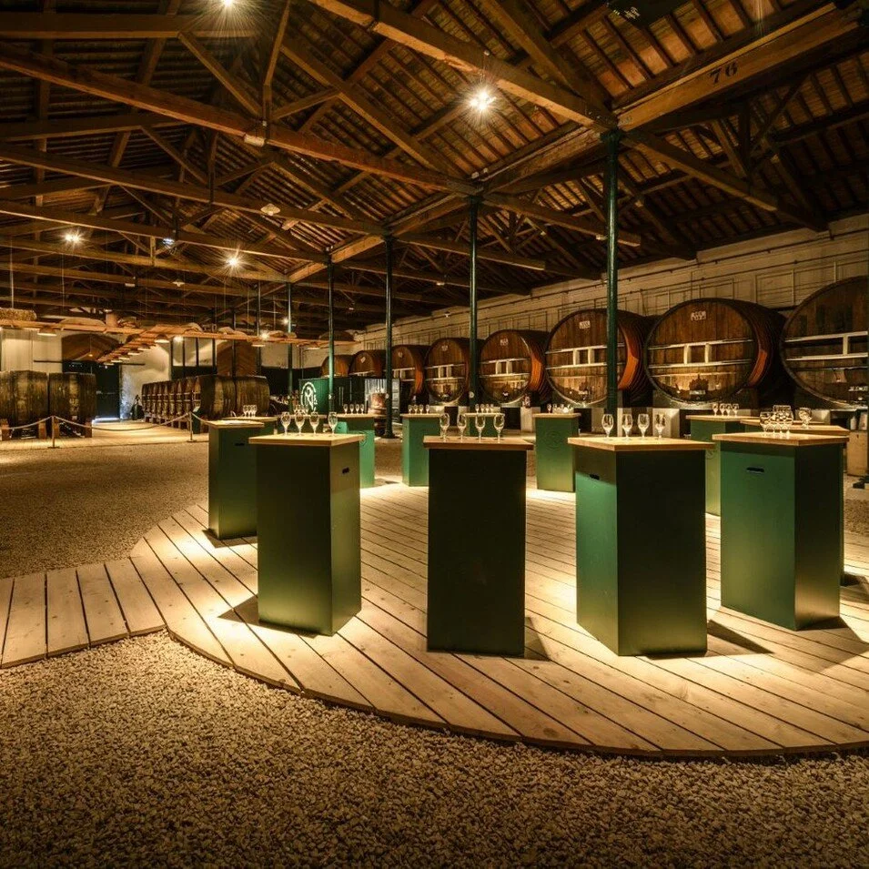 Salle de dégustation de vin avec tonneaux en bois, tables avec des verres à vin, ambiance chaleureuse et éclairage doux.