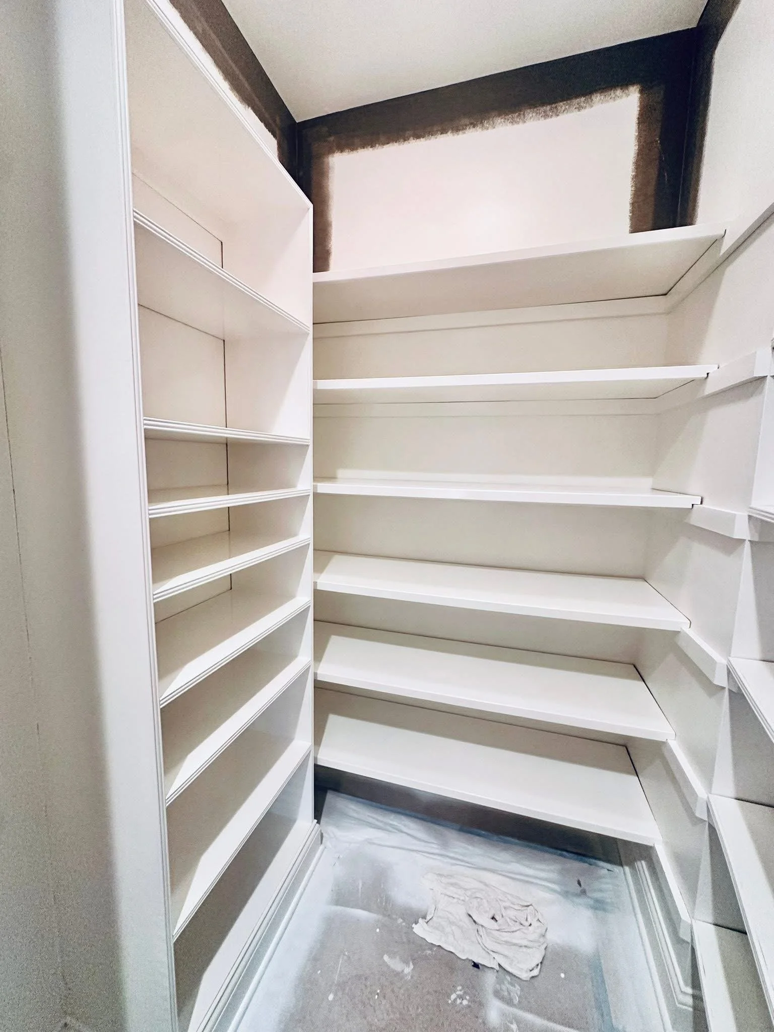 Empty white walk-in closet with shelves and rods, construction dust on the floor, and an unfinished wall at the top.