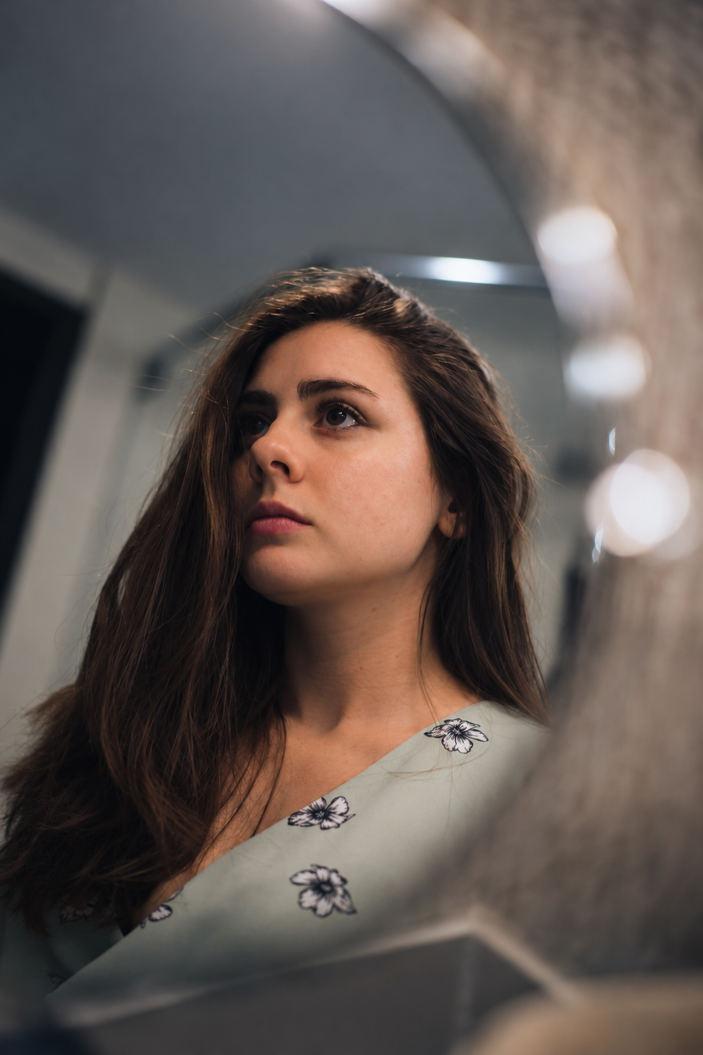 Une jeune femme aux longs cheveux bruns regarde pensivement dans un miroir.
