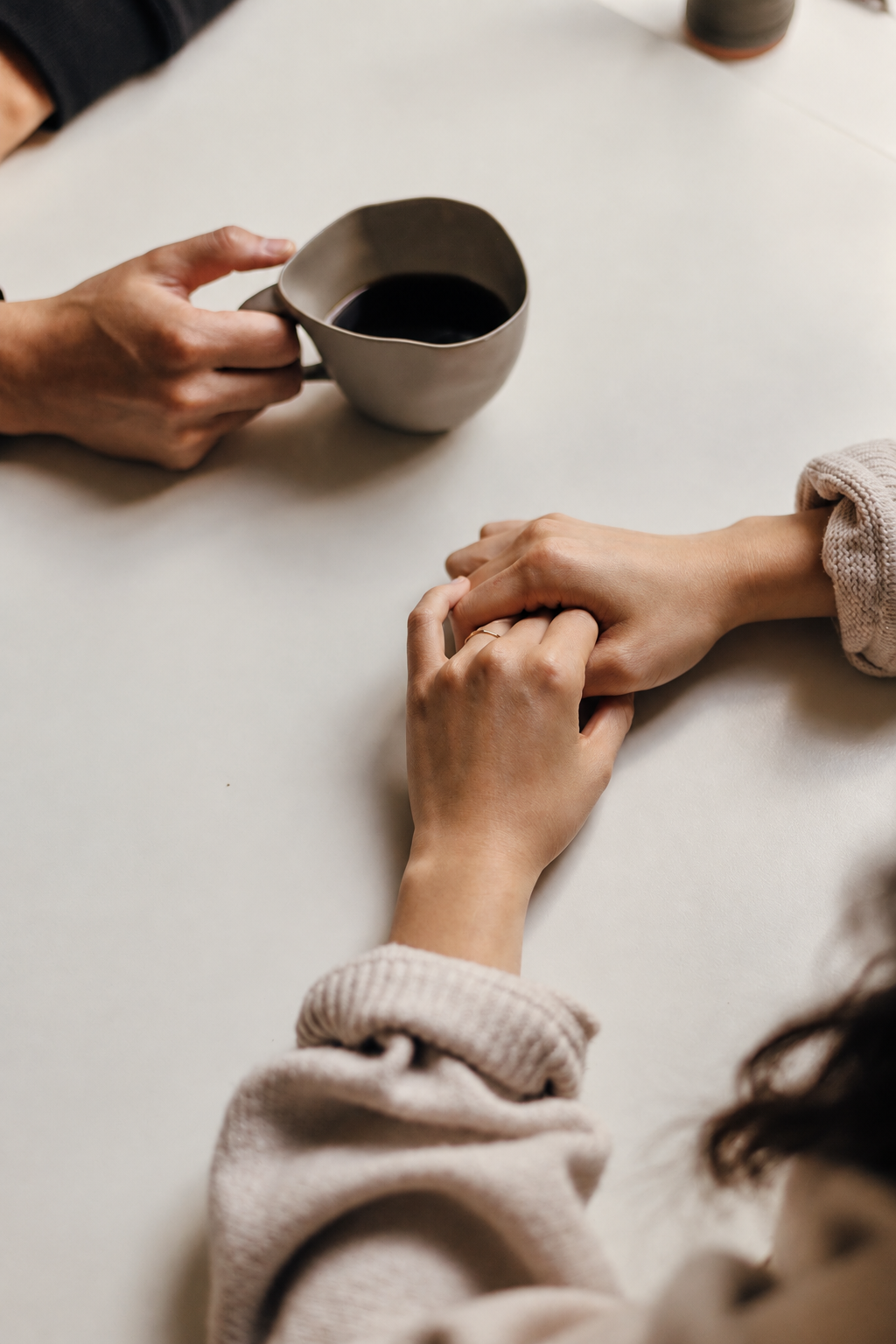 Deux mains qui se tiennent, une femme et un homme, avec une tasse de café ou de thé sur une table blanche