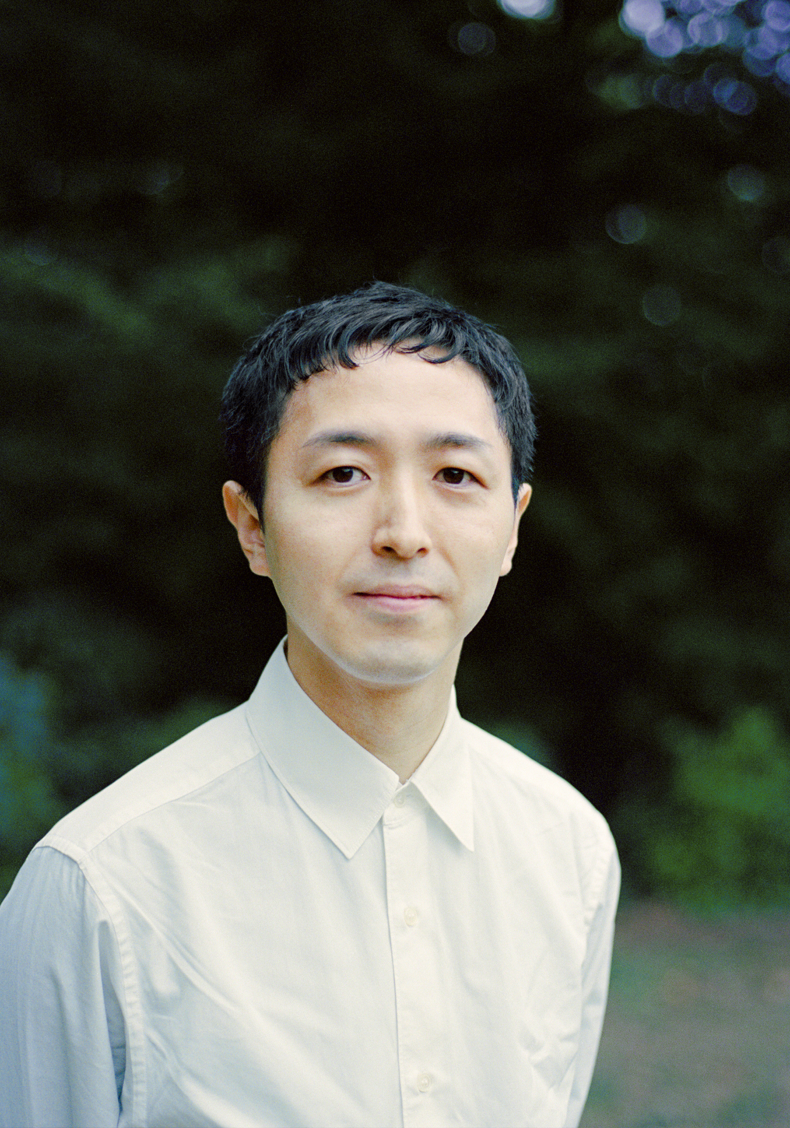 白いシャツを着た男性のポートレート、背景は緑の木々とぼやけた青い光