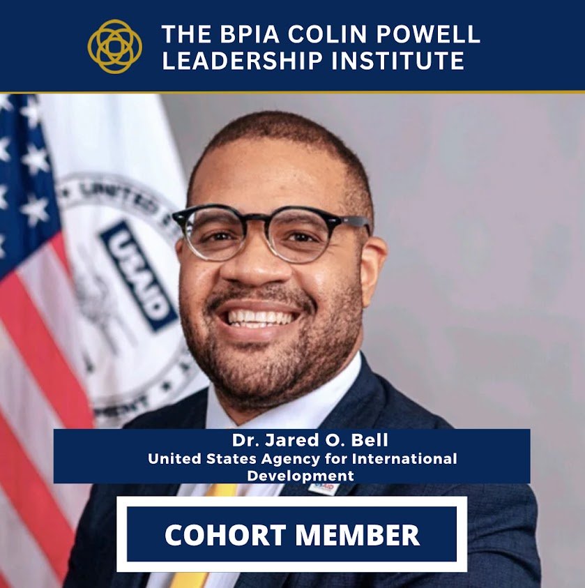 A professional headshot of Dr. Jared O. Bell, smiling, wearing glasses and a suit, with flags and an official seal in the background. The image promotes the Biden Harris Poverty to Prosperity Leadership Institute at the Colin Powell Leadership Institute, indicating he is a cohort member.