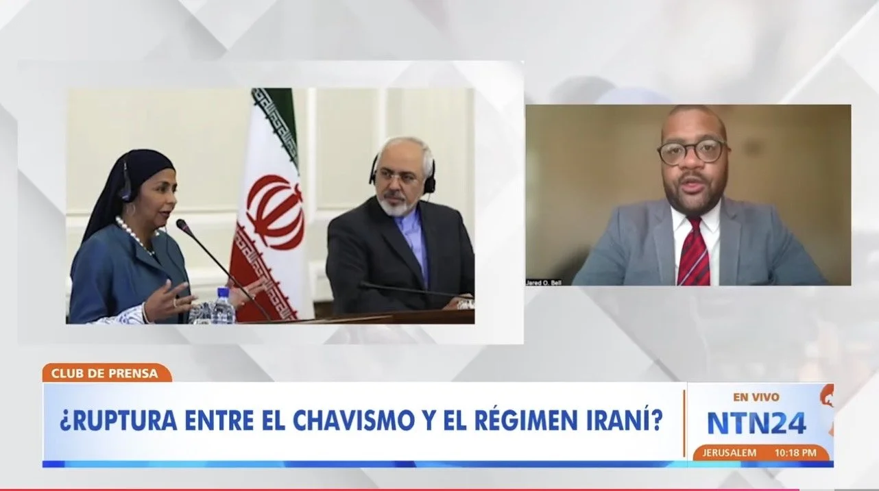 A news broadcast showing a split screen with a woman and a man in a formal setting on the left, and a man in a suit and glasses speaking from a different location on the right. The background includes the Iranian flag and a news ticker in Spanish.