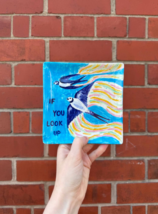 Colorful painted tile featuring two flying birds and the text "If you look up," in front of a brick wall.