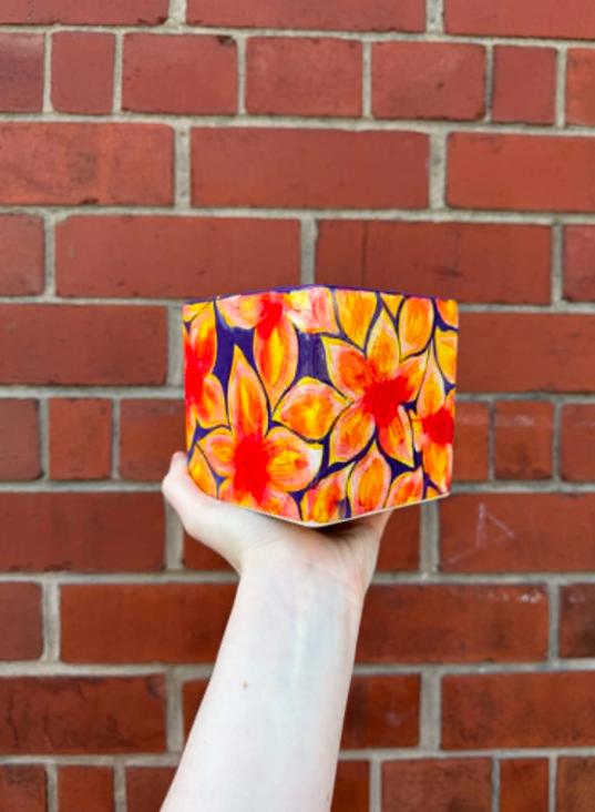 Hand holding a colorful floral decorated cube with a brick wall in the background.